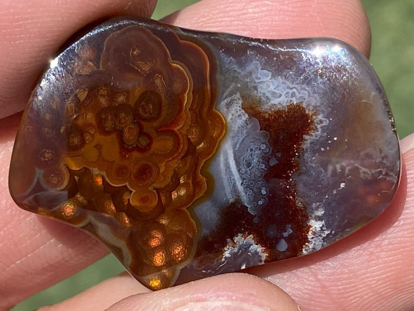 Bottom of a polished Slaughter Mountain fire agate gemstone held between fingers.