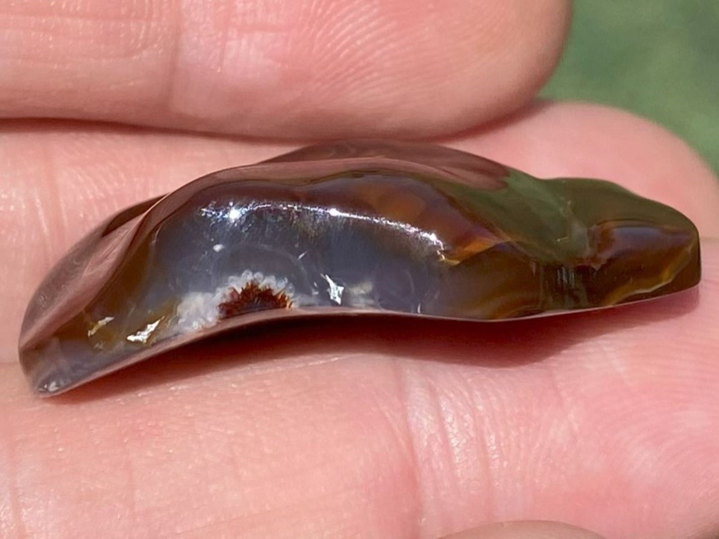 Translucent brown stone held between fingers showing a slightlly curved bottom of the gemstone.