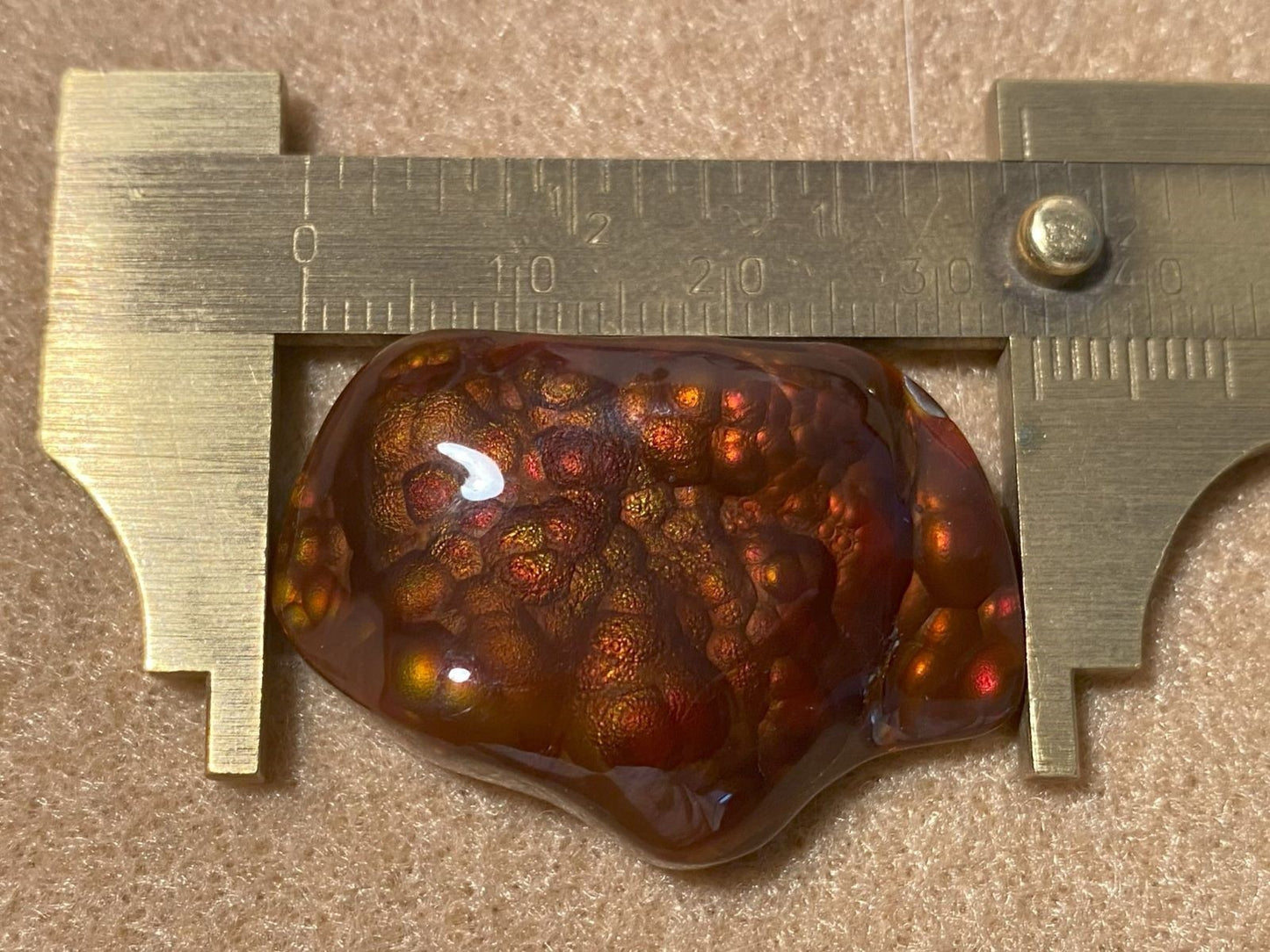 Slaughter Mountain fire agate gemstone with a ruler for scale which measures 33 mm on a beige background.