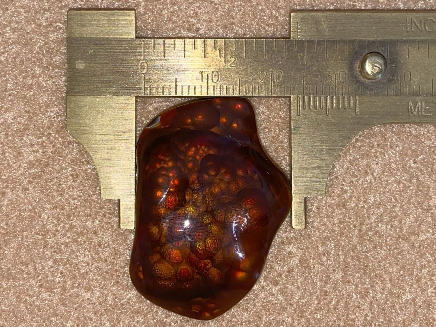 Multi-colored fire agate gemstone with a metallic ruler which shows it measuring 23 mm.