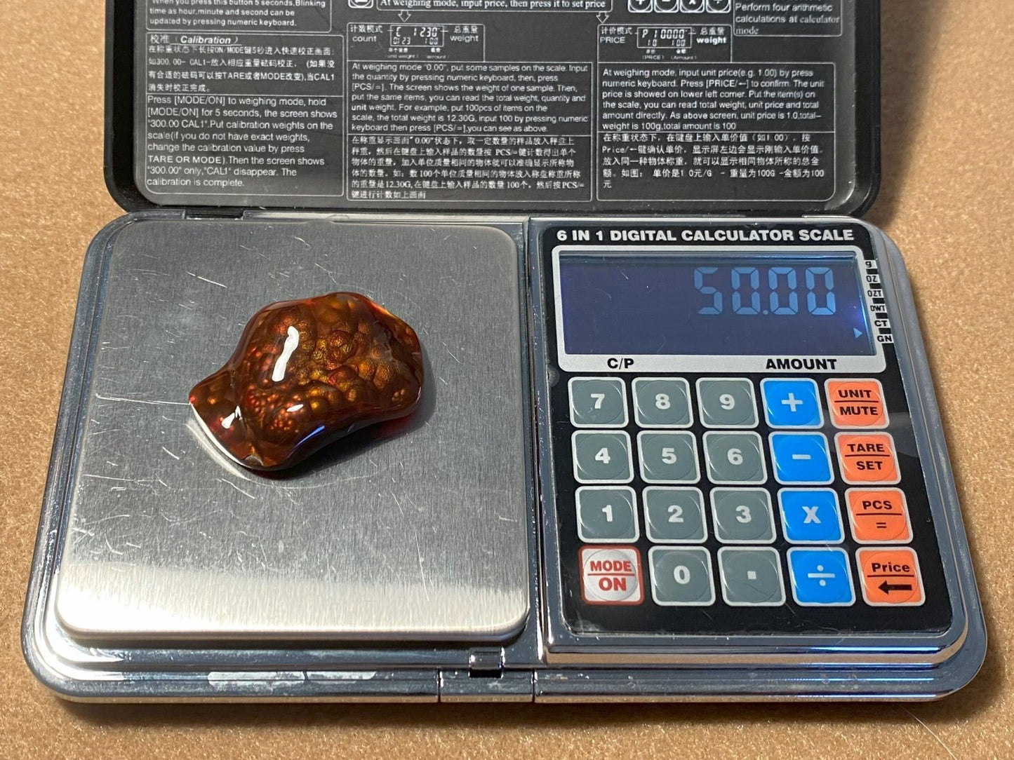 Calculator scale with a Slaughter Mountain fire agate gemstone on it, displaying a weight reading of 50 carats.