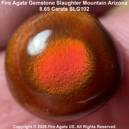 A close-up of a polished fire agate gemstone held against a person's fingers, showing a vibrant orange and red fiery pattern on a brown translucent background. Text overlays identify the stone as 'Fire Agate Gemstone Slaughter Mountain Arizona'.