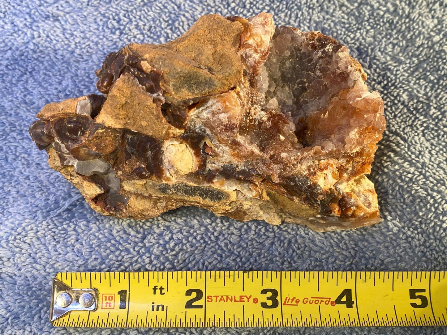 Slaughter Mountain fire agate rough mineral specimen with a measuring tape for scale on a textured surface