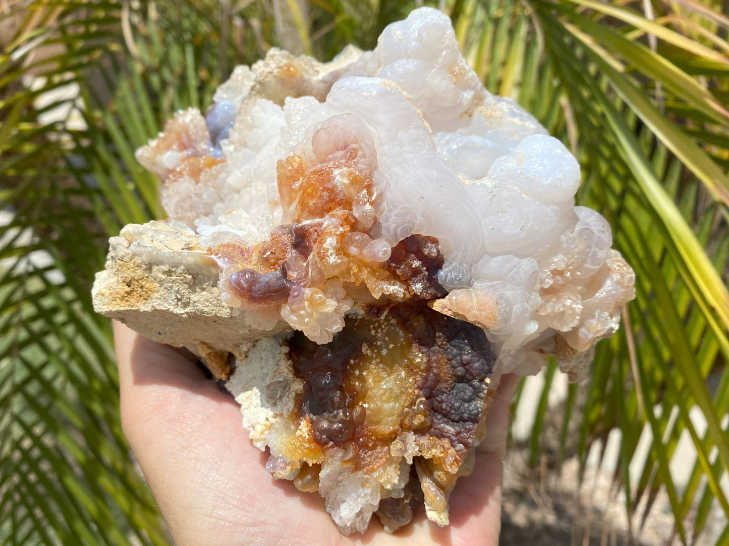 Hand holding a large piece of Slaughter Mountain fire agate rough with crystal formation and a natural background