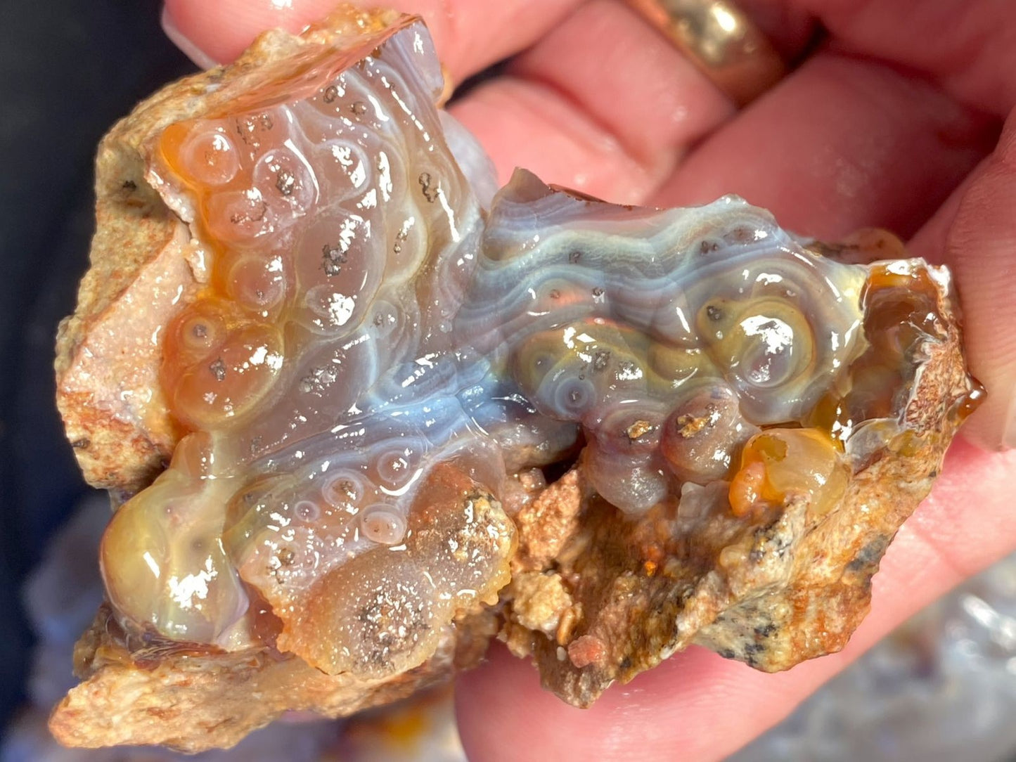Close-up of a hand holding a piece of fire agate with visible patterns