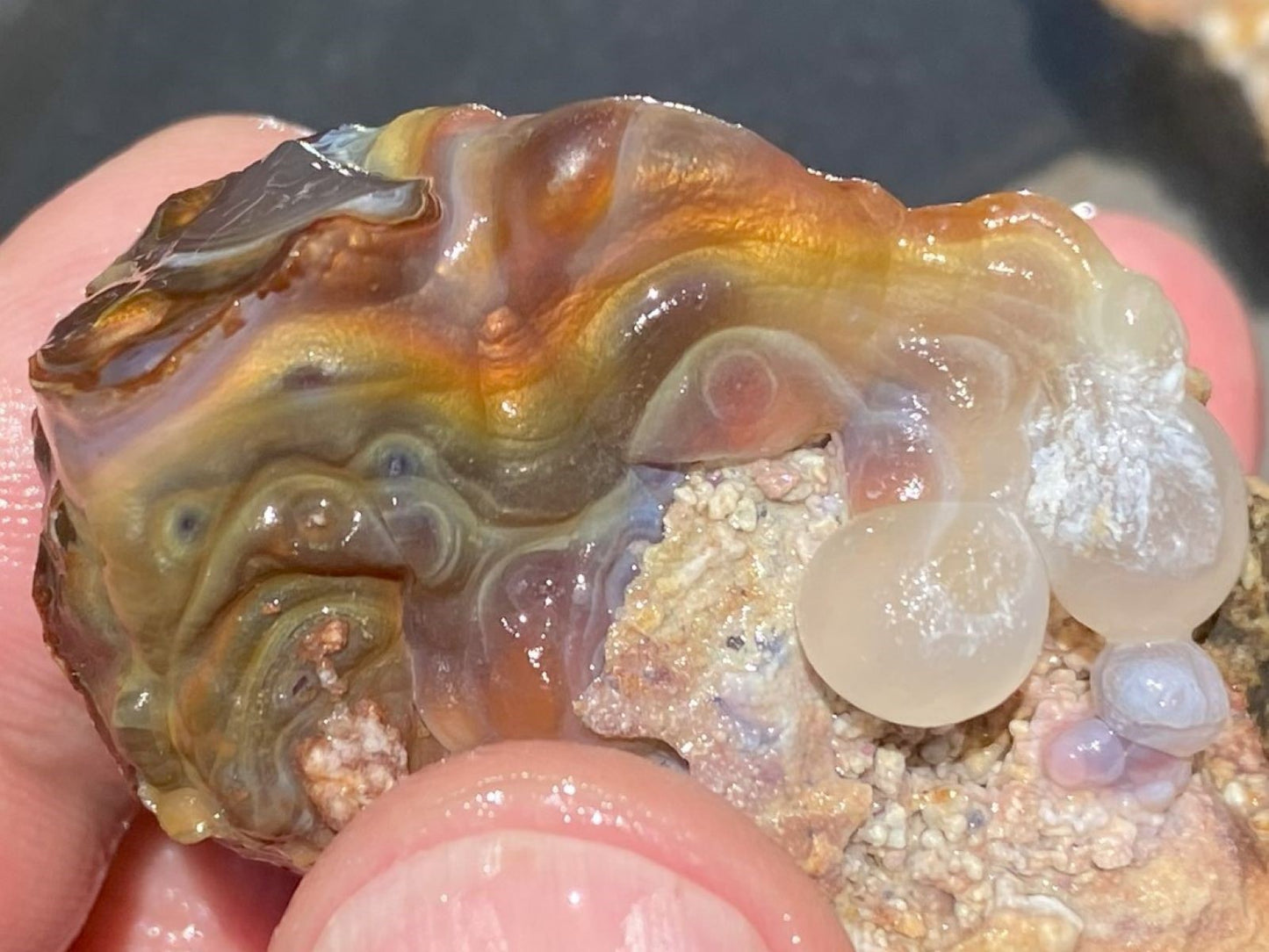 Close-up of a colorful Slaughter Mountain fire agate stone held between fingers