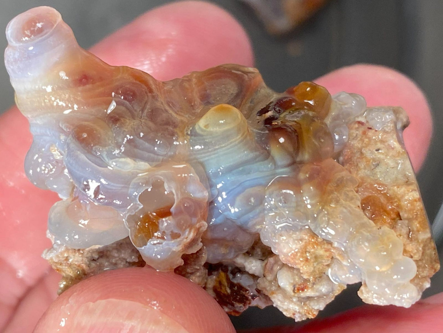 Close-up of a translucent crystal-like piece of Slaughter Mountain fire agate rough held between fingers