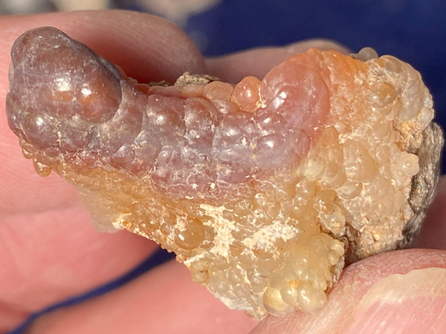 Close-up of a textured piece of Slaughter Mountain fire agate rough held between fingers with a blurred background