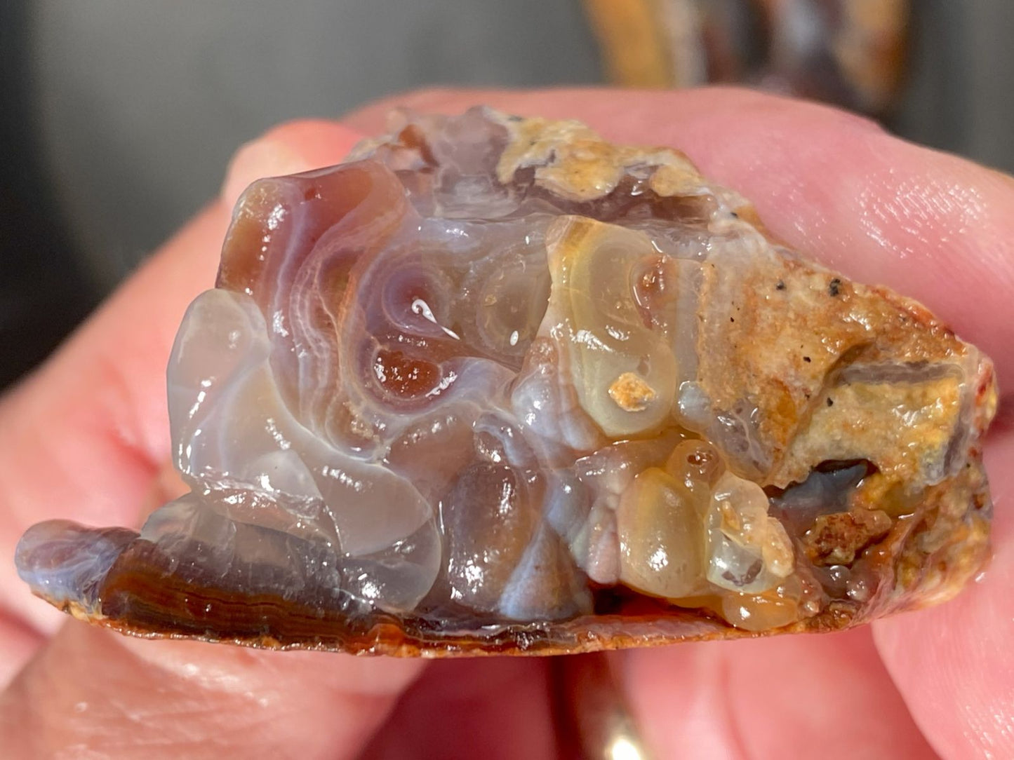 Close-up of a hand holding a piece of Slaughter Mountain fire agate rough with visible layers and colors.