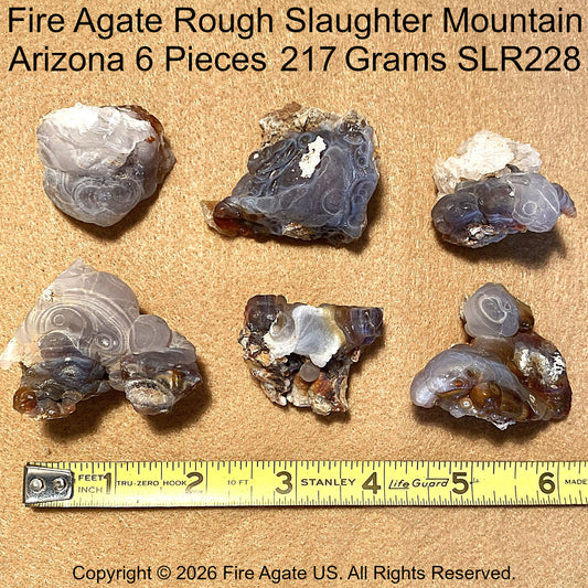 Six pieces of rough fire agate displayed on a tan textured background with a yellow measuring tape at the bottom for scale. Text at the top reads 'Fire Agate Rough Slaughter Mountain Arizona 6 Pieces 217 Grams SLR228' and a copyright notice for Fire Agate US is at the bottom.