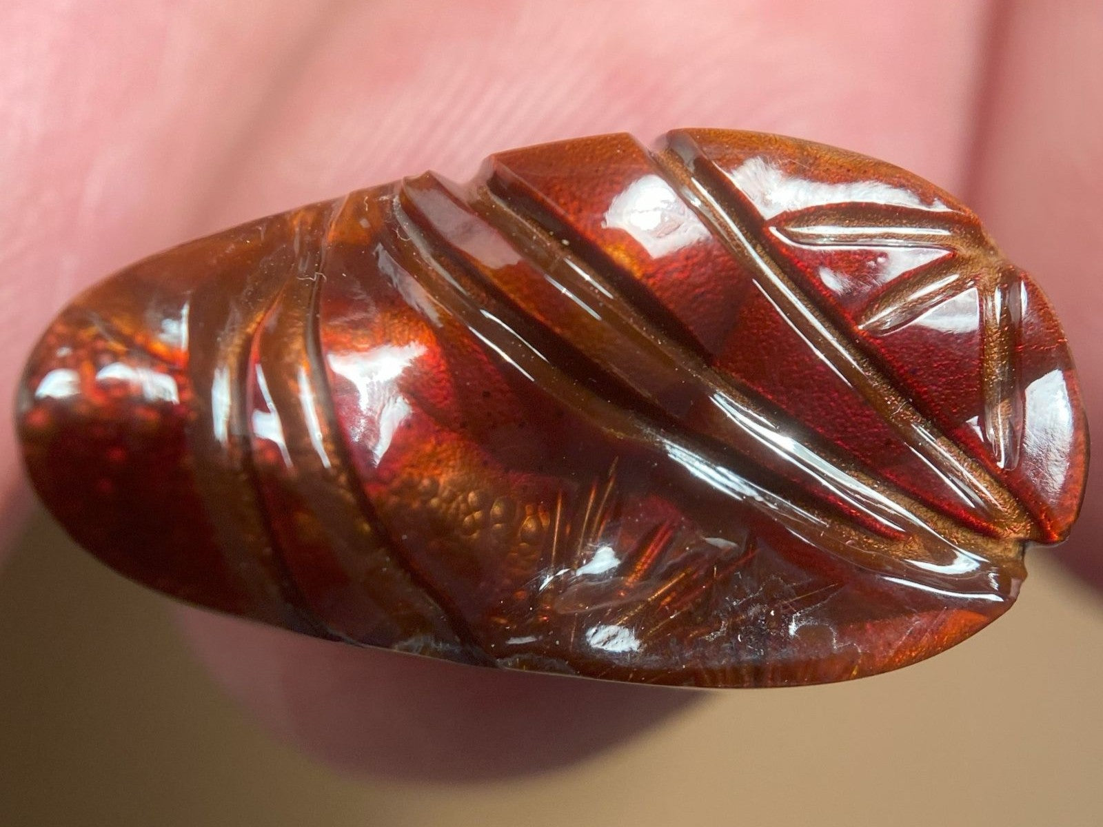 Close-up of a polished burgundy red, orane and brown Slaughter Mountain fire agate gem held between fingers