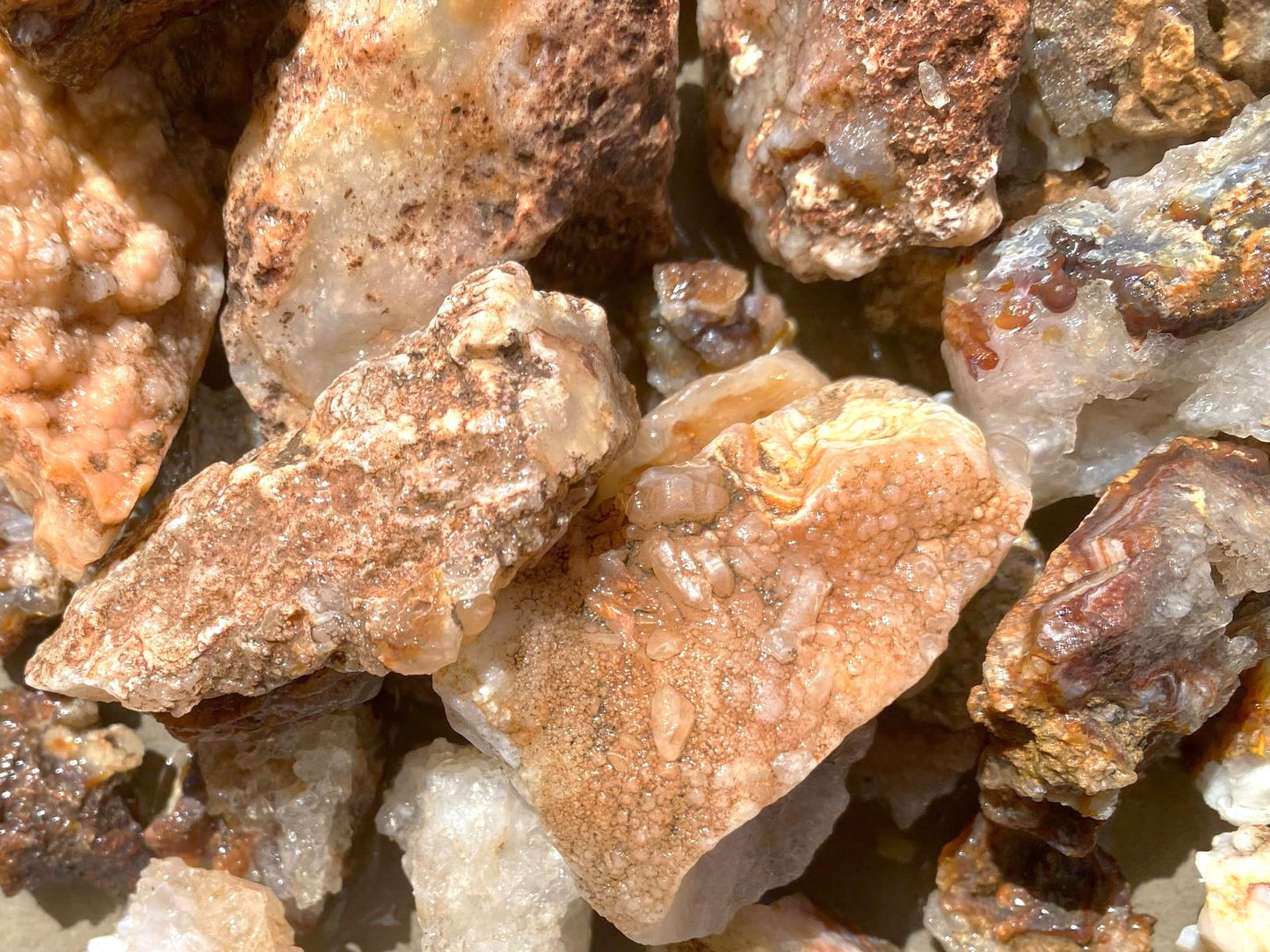 A close-up pile of rough mineral and rock specimens with tan, brown, cream, and translucent white crystalline areas.