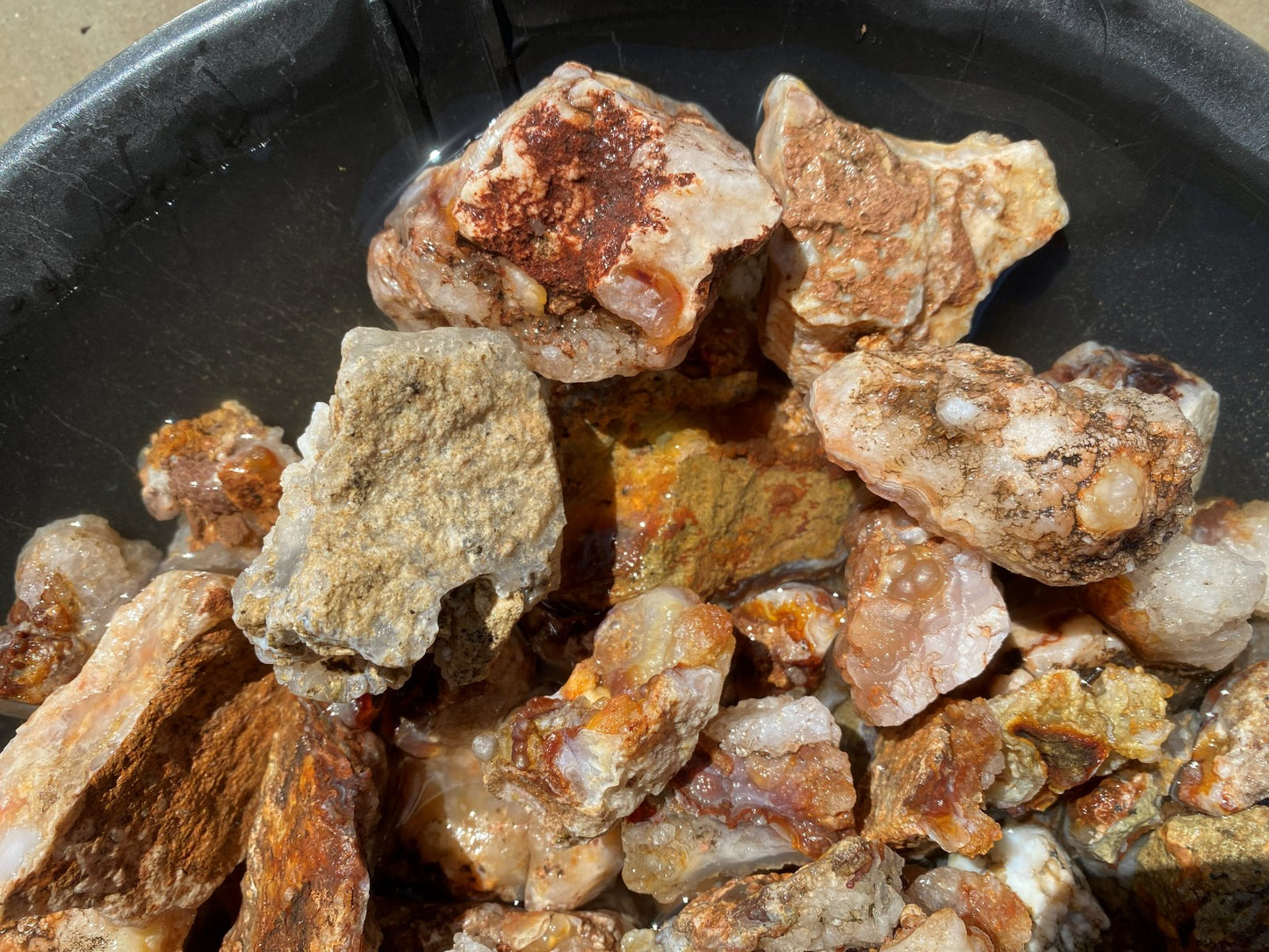 A close-up pile of rough mineral or stone chunks with orange, tan, brown, and translucent qualities, resting inside a dark bowl.
