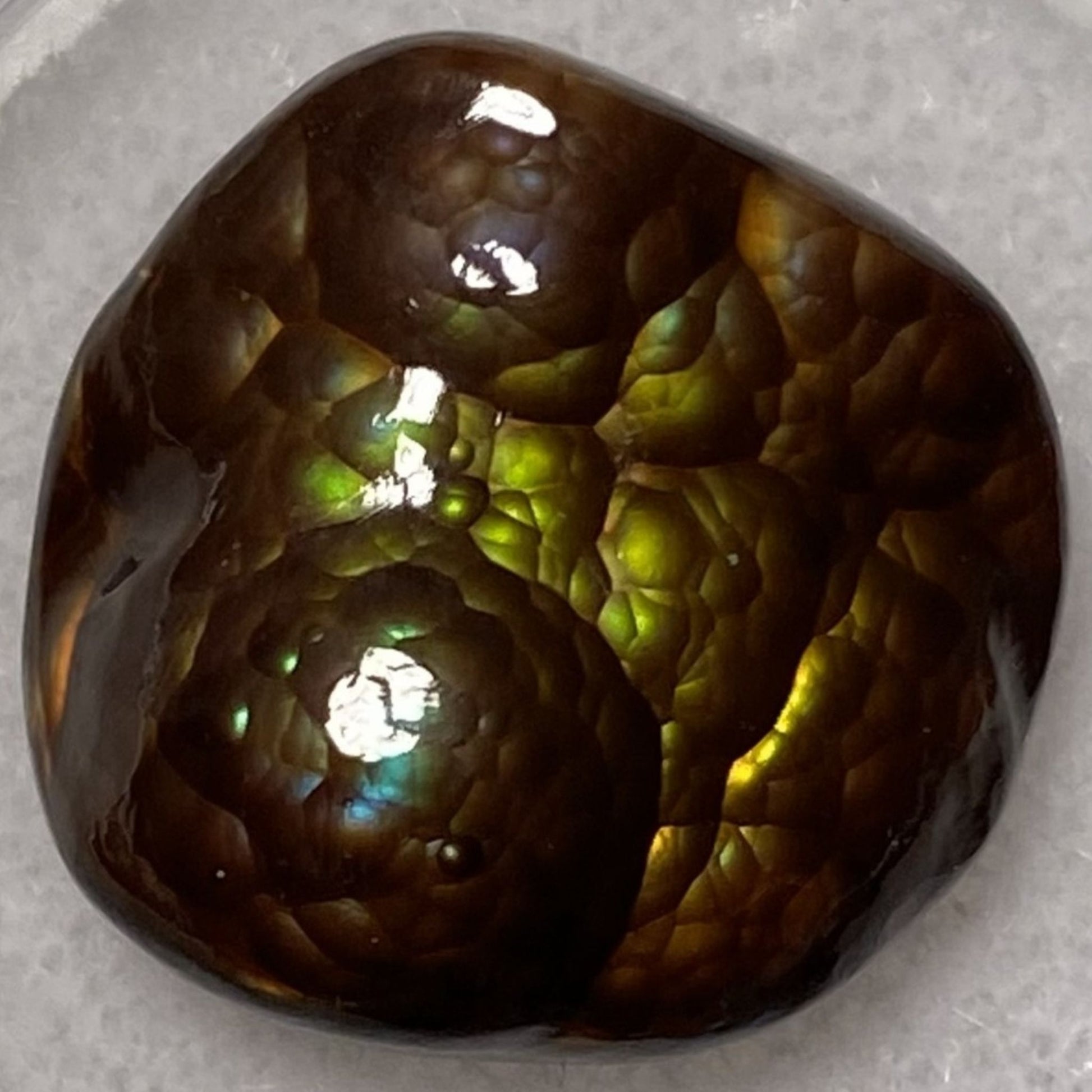 Close-up of a polished  colorful Deer Creek fire agate gemstone with green and brown colors on a gray background