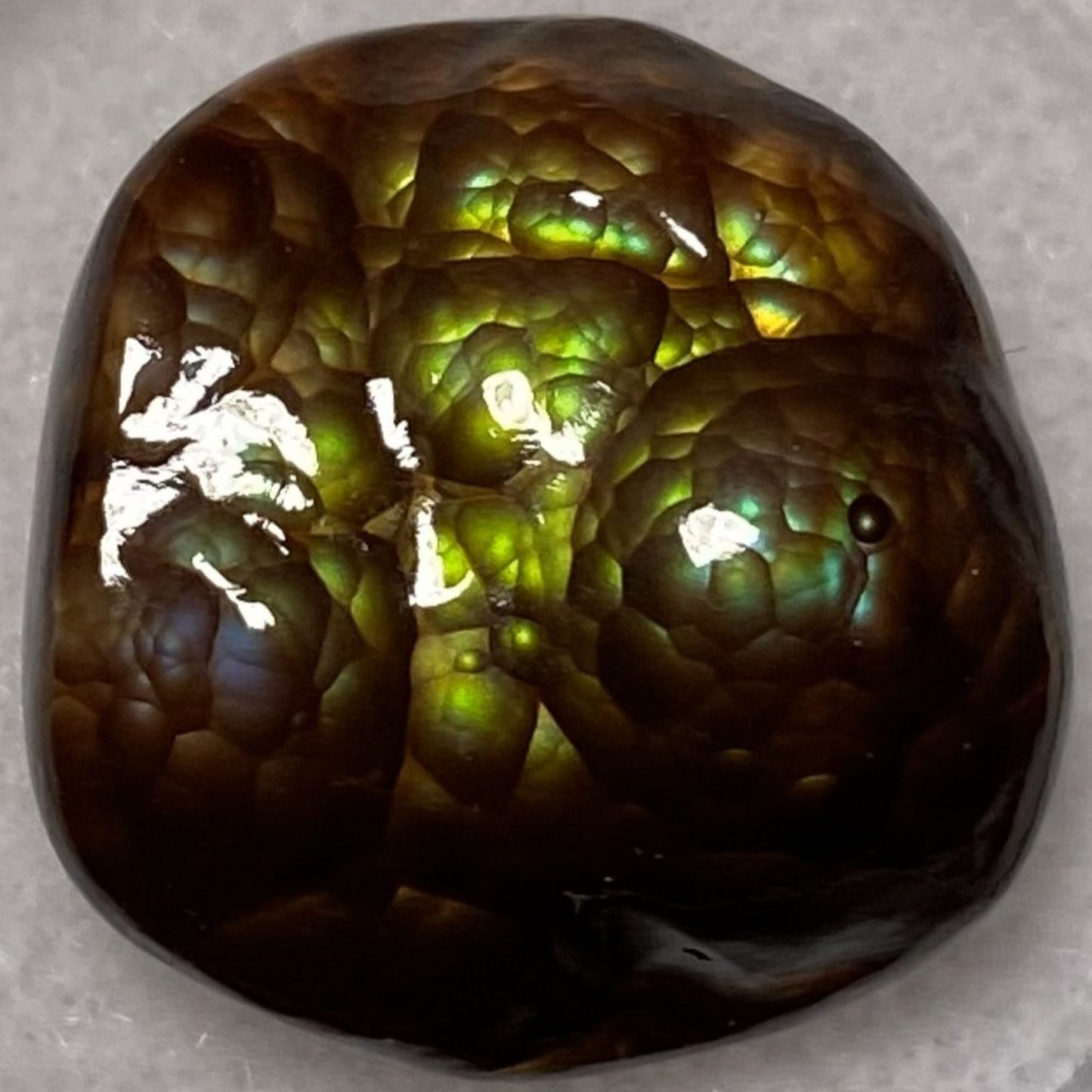 Close-up of a polished Deer Creek Arizona fire agate gemstone with green and brown colors on a gray background