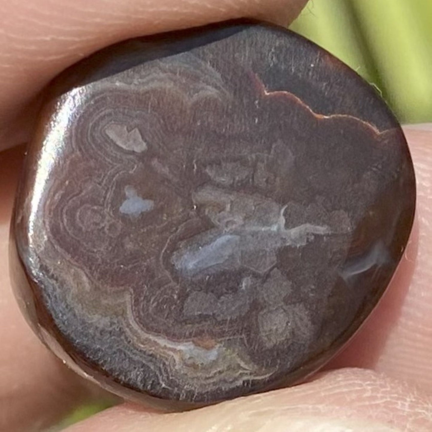 Close-up of bottom of a fire agate gem with intricate patterns held in a hand.