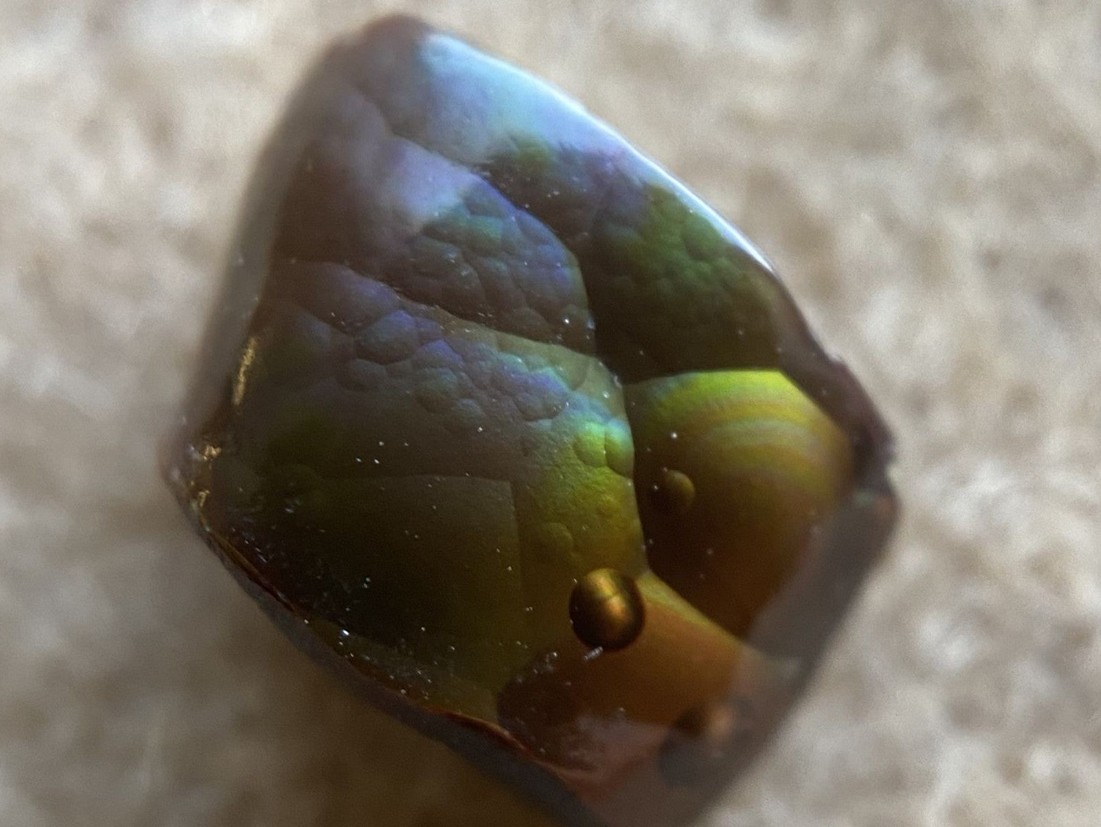 Multicolored Deer Creek fire agate gemstone on a beige surface