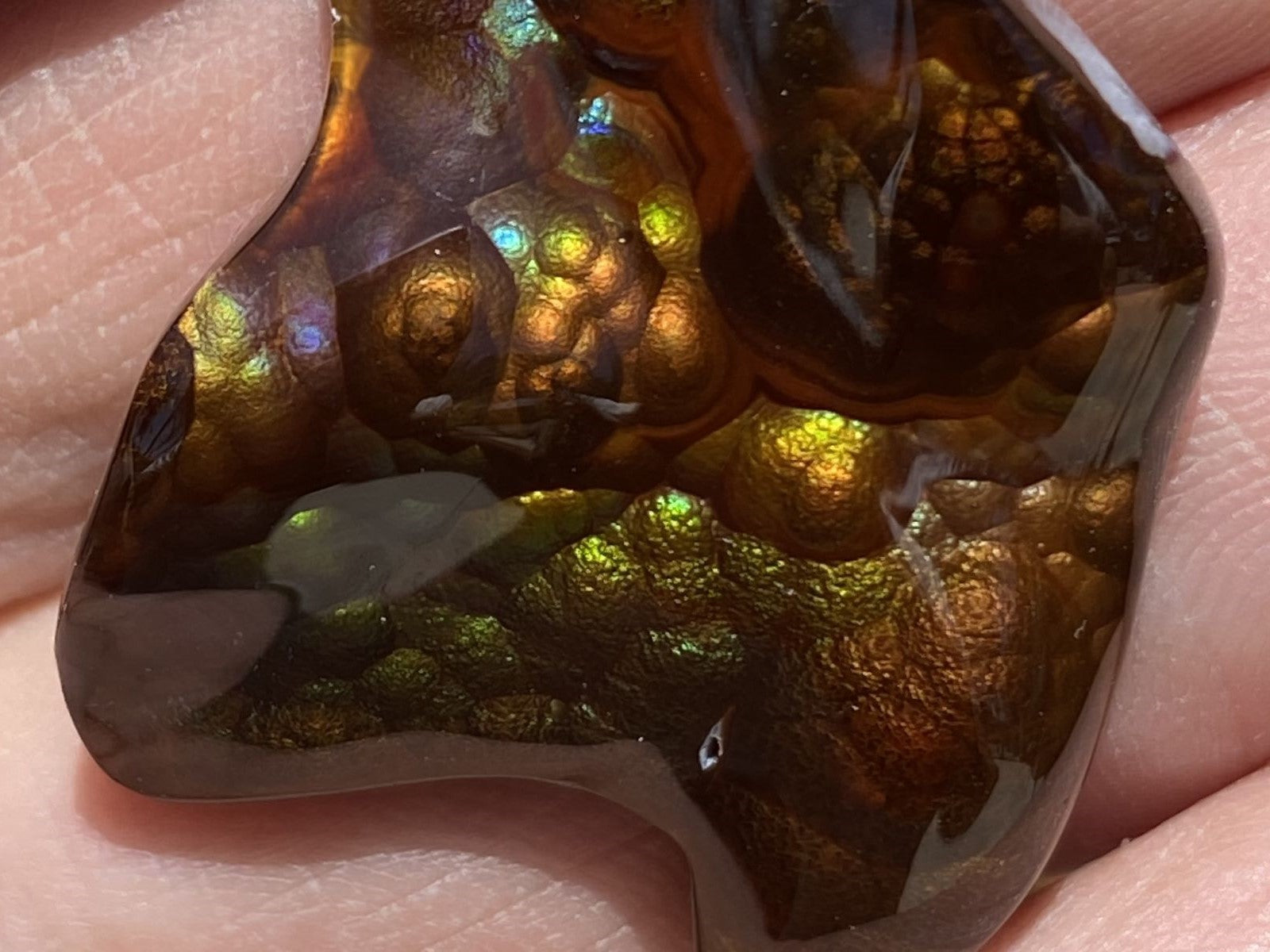 Close-up of a polished Deer Creek fire agate gemstone held between fingers