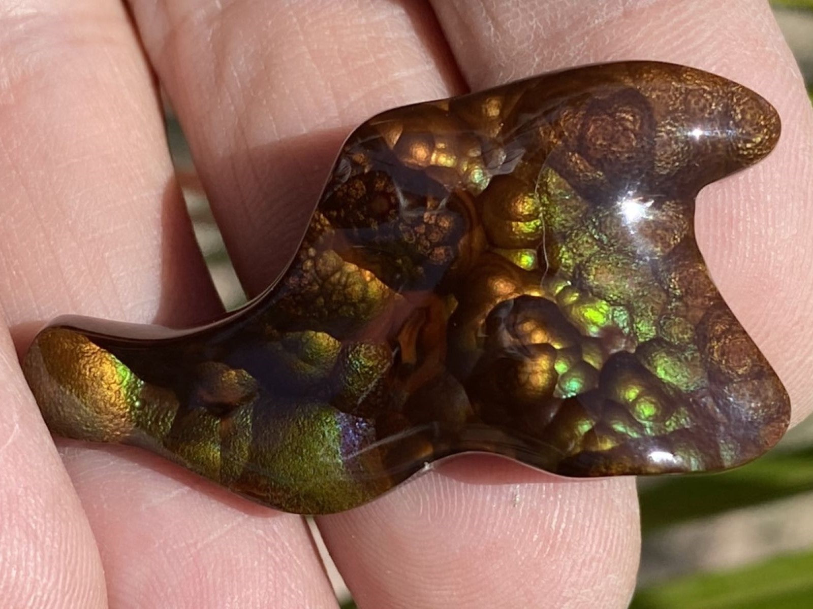 A colorful Deer Creek fire agate gemstone held between fingers with a natural background