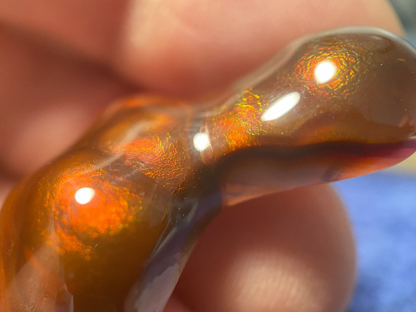 Close-up of a Deer Creek fire agate gemstone showing orange, red and green fire held by a hand.