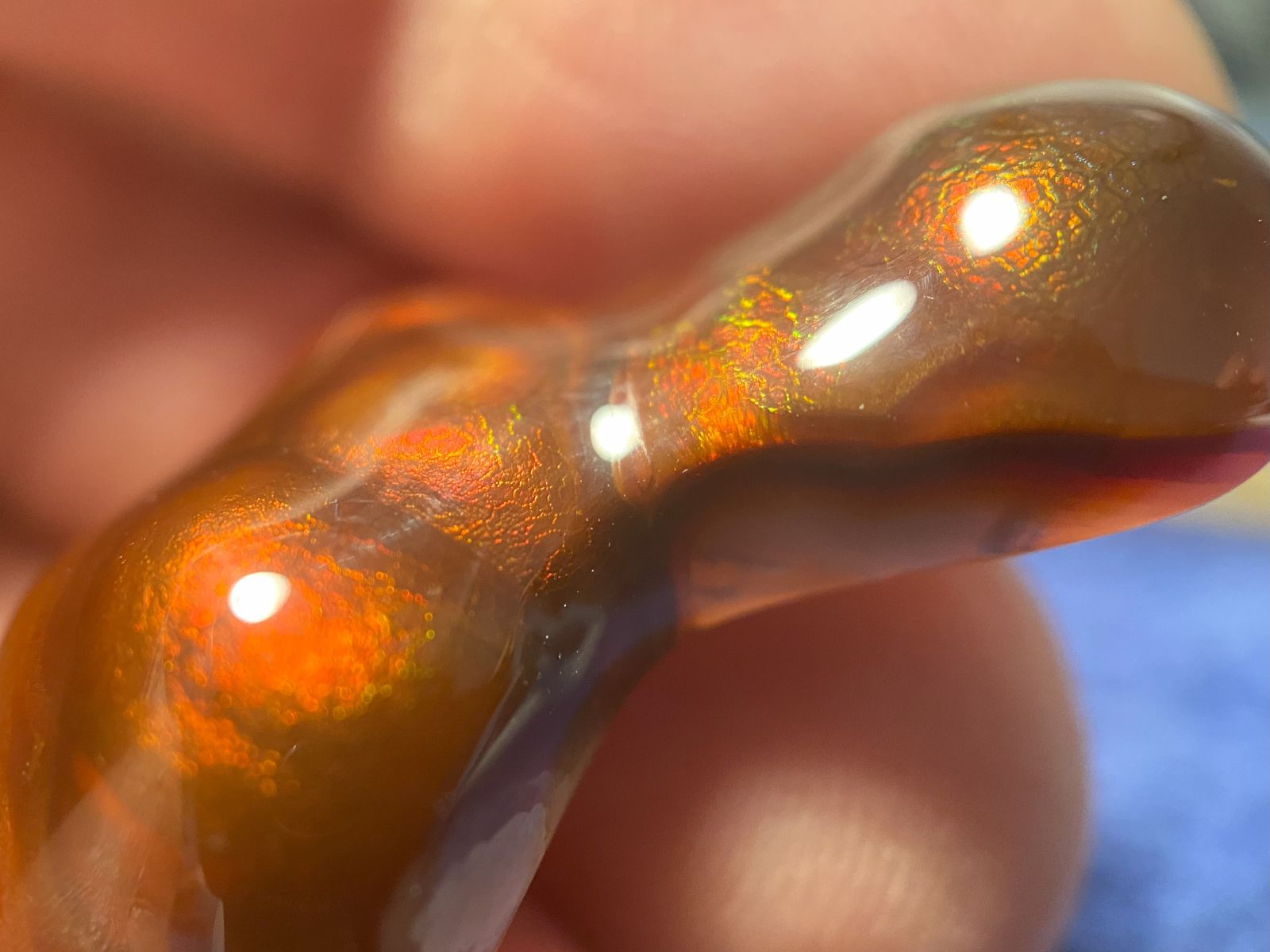 Close-up of a Deer Creek fire agate gemstone showing orange, red and green fire held by a hand.