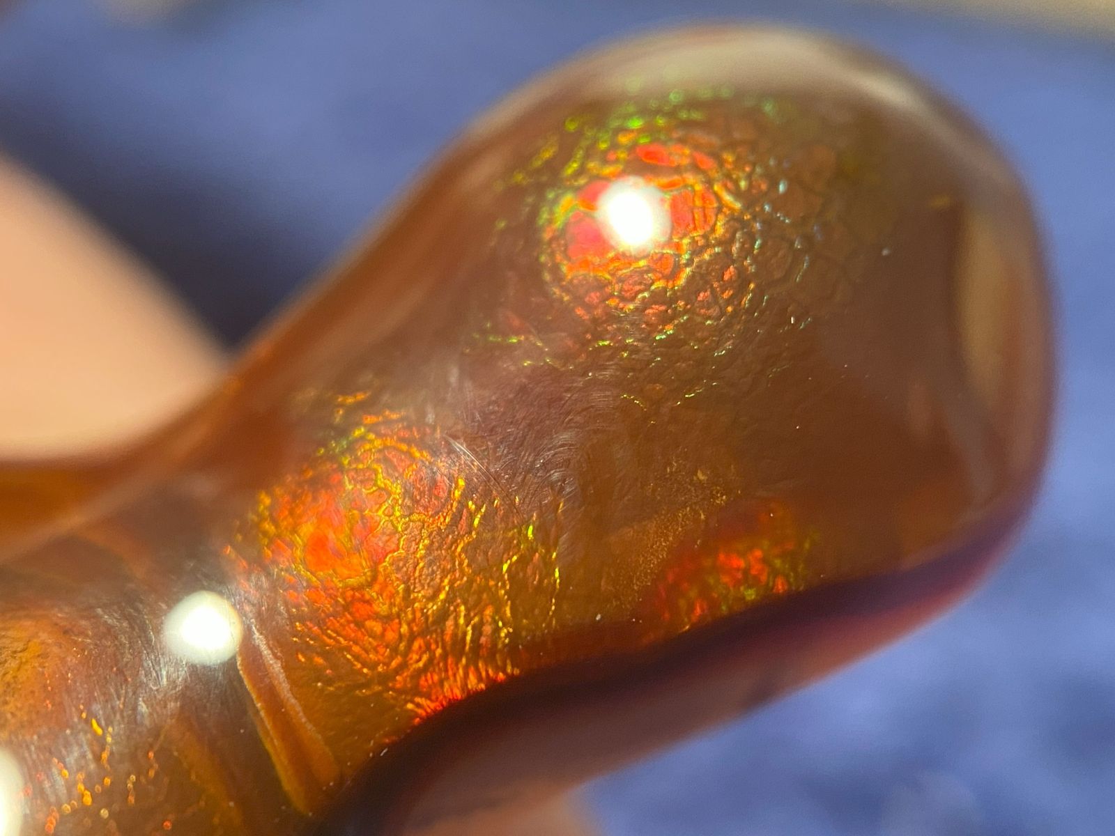 Close-up of a piece of fire agate gemstone with an iridescent red and green crackle patterns on a blurred background.