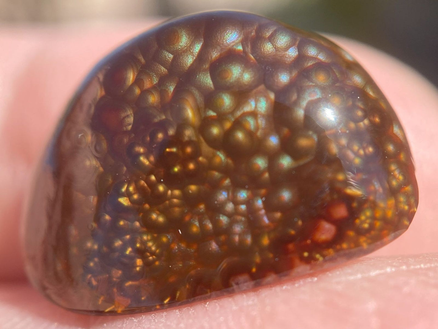 Close-up of a Deer Creek Fire Agate Gemstone with a textured surface held between fingers.