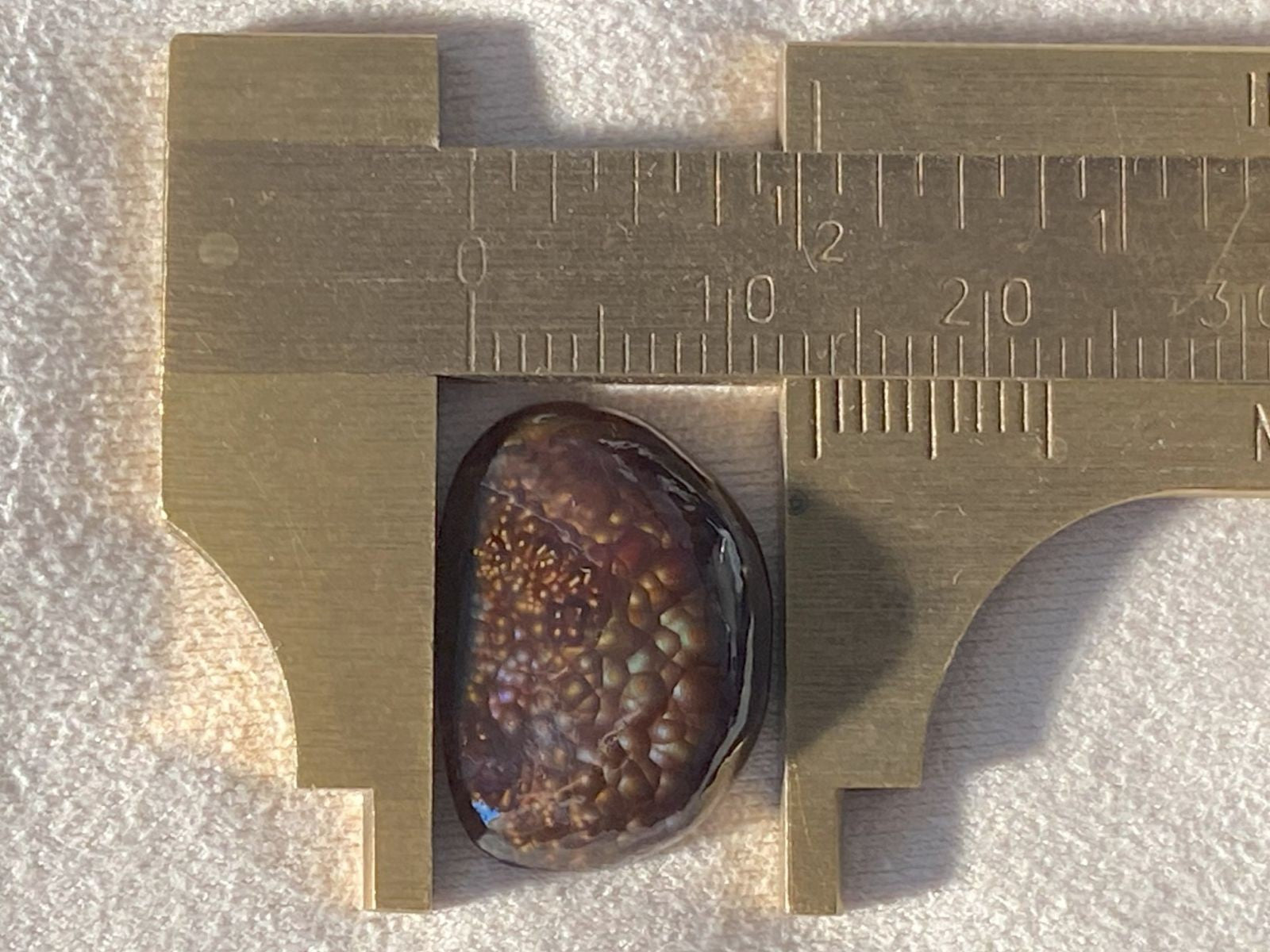 Deer Creek Fire Agate Gemstone with a vernier caliper on a textured surface