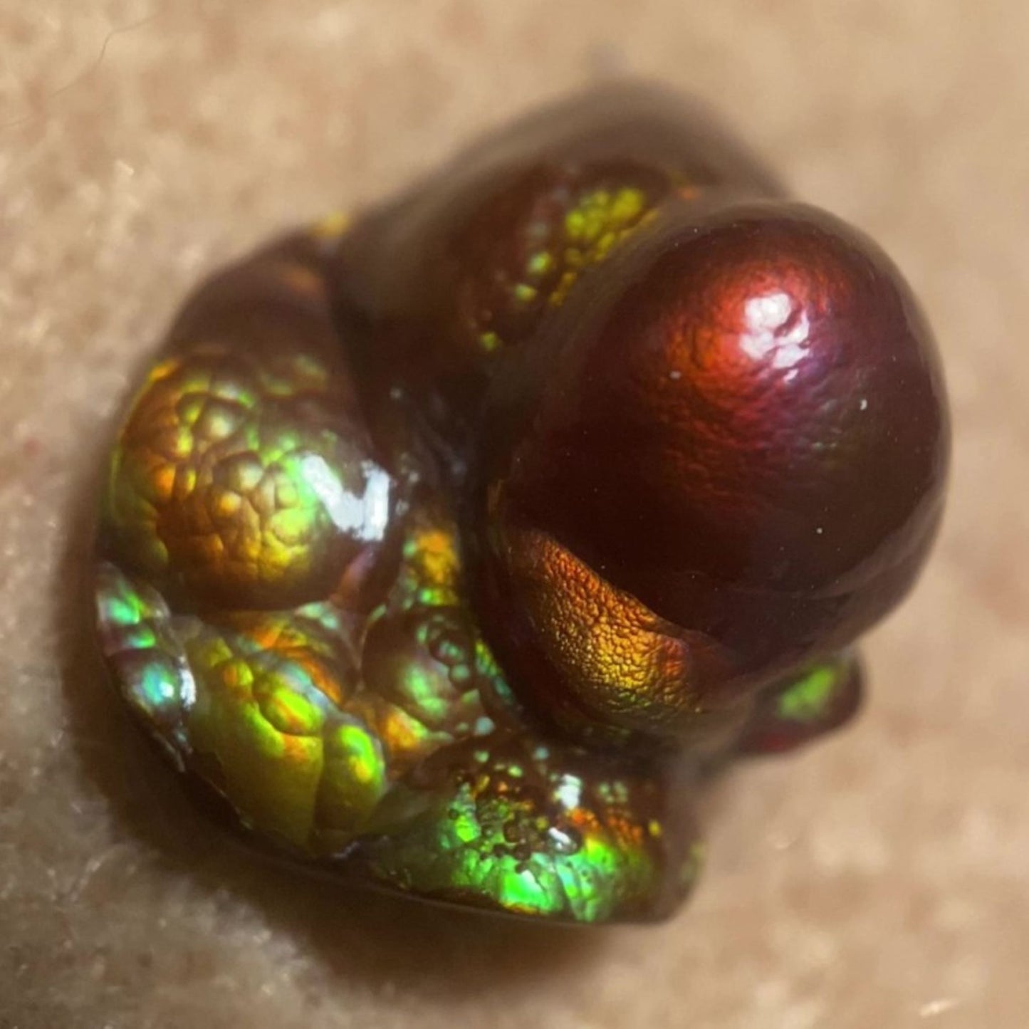 Close-up of a colorful Deer Creek iridescent Fire Agate Gemstone Thumbnail Mineral Specimen on a beige background