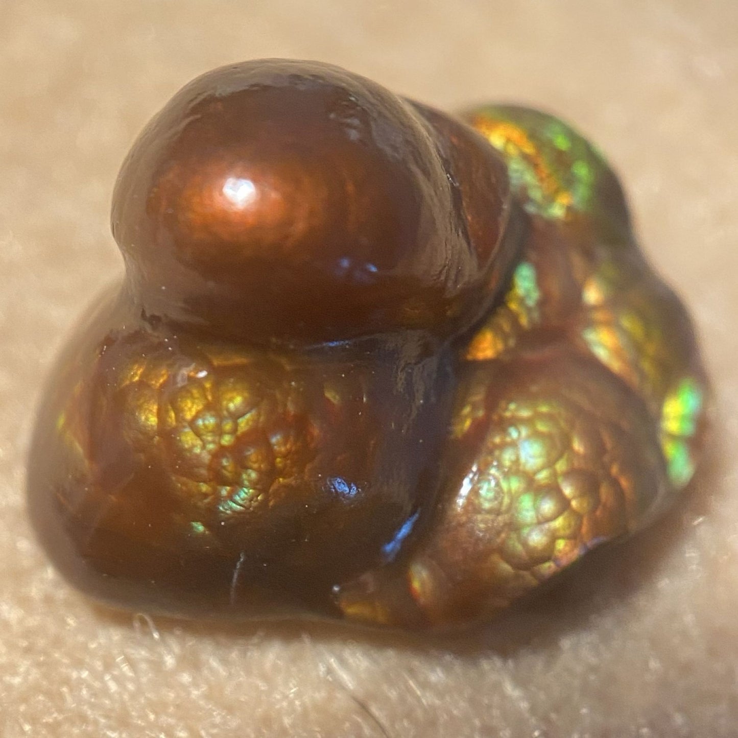 Deer Creek iridescent Fire Agate Gemstone Thumbnail Specimen displaying multicolored play of light on a beige background