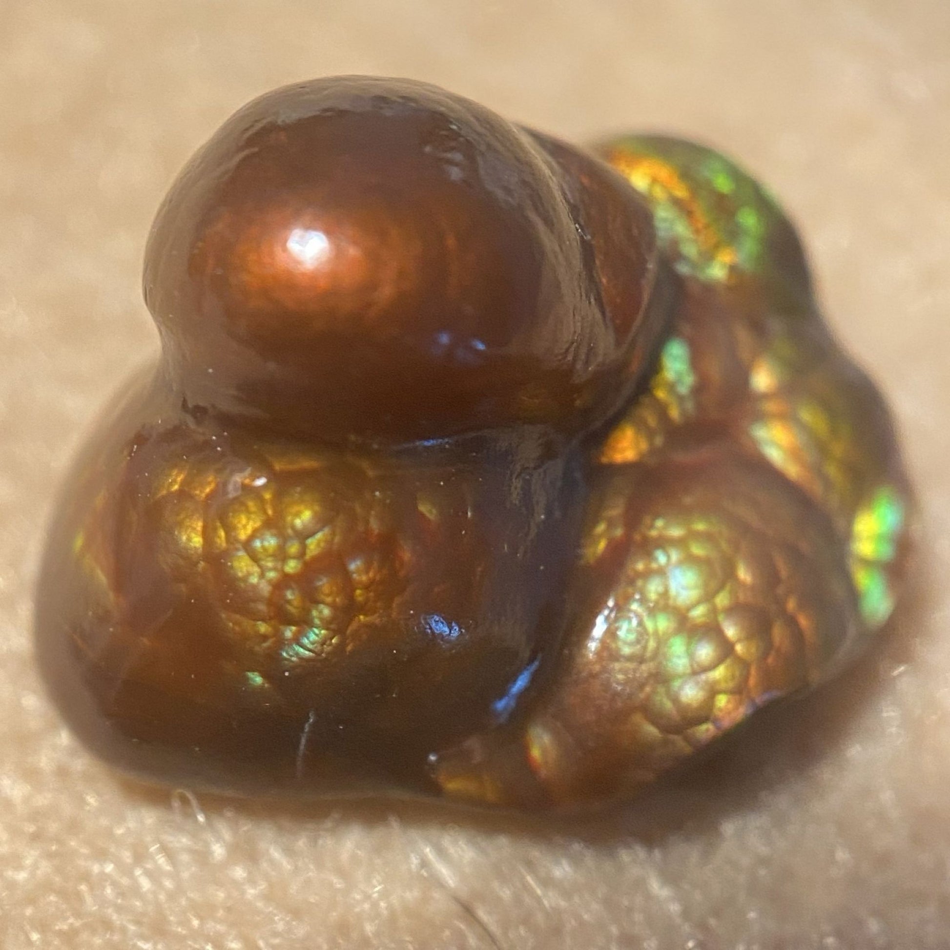 Deer Creek iridescent Fire Agate Gemstone Thumbnail Specimen displaying multicolored play of light on a beige background