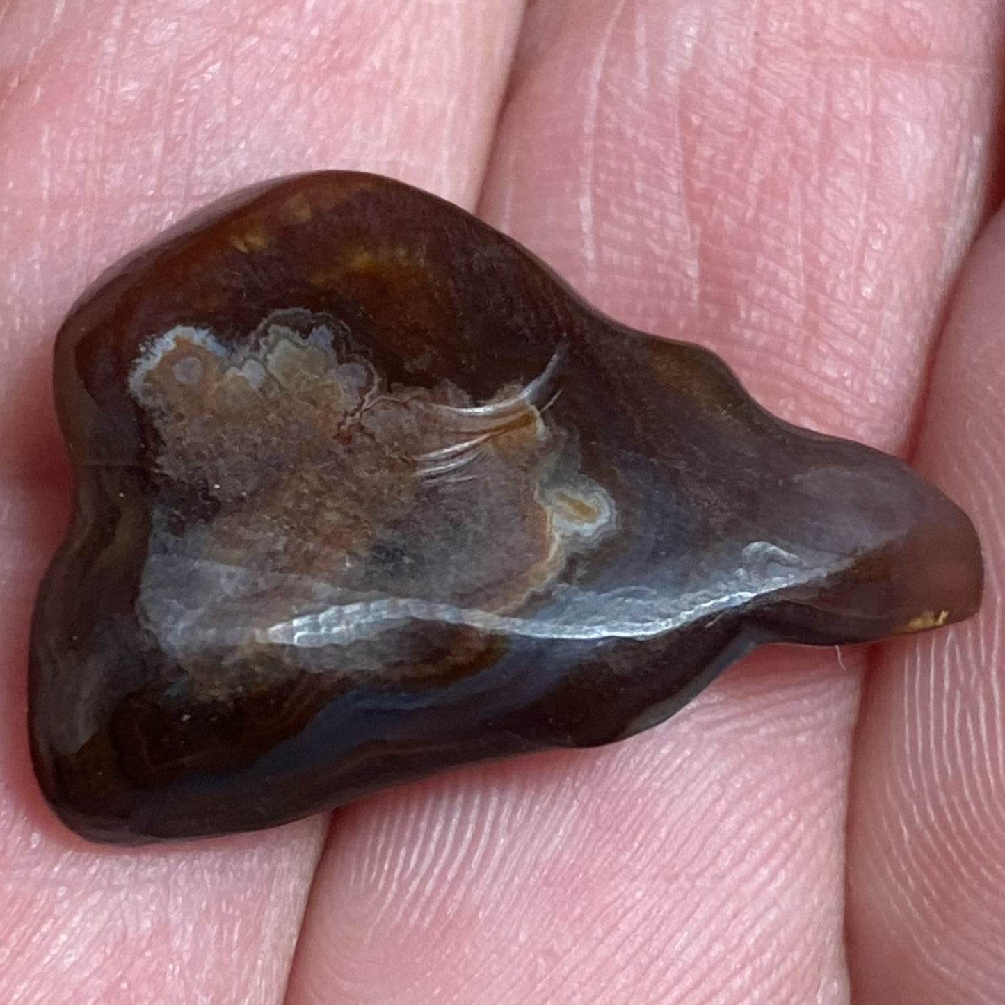 Bottom of a Deer Creek Fire Agate Gemstone with a unique pattern held between fingers