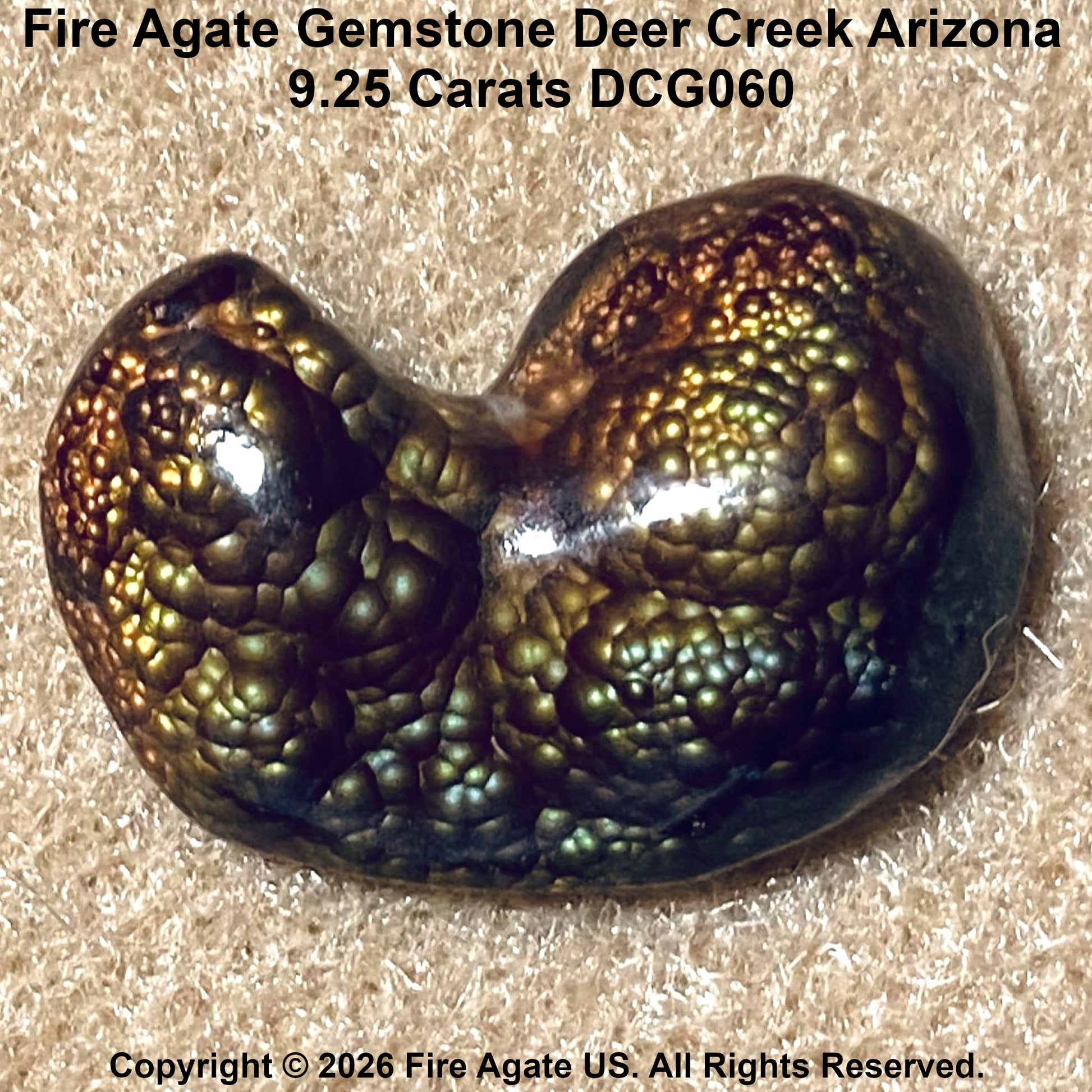 A polished fire agate gemstone with a biconical shape, displaying a textured, bubble-like surface in iridescent green, bronze, and black tones, resting on a beige textured background with product details text.