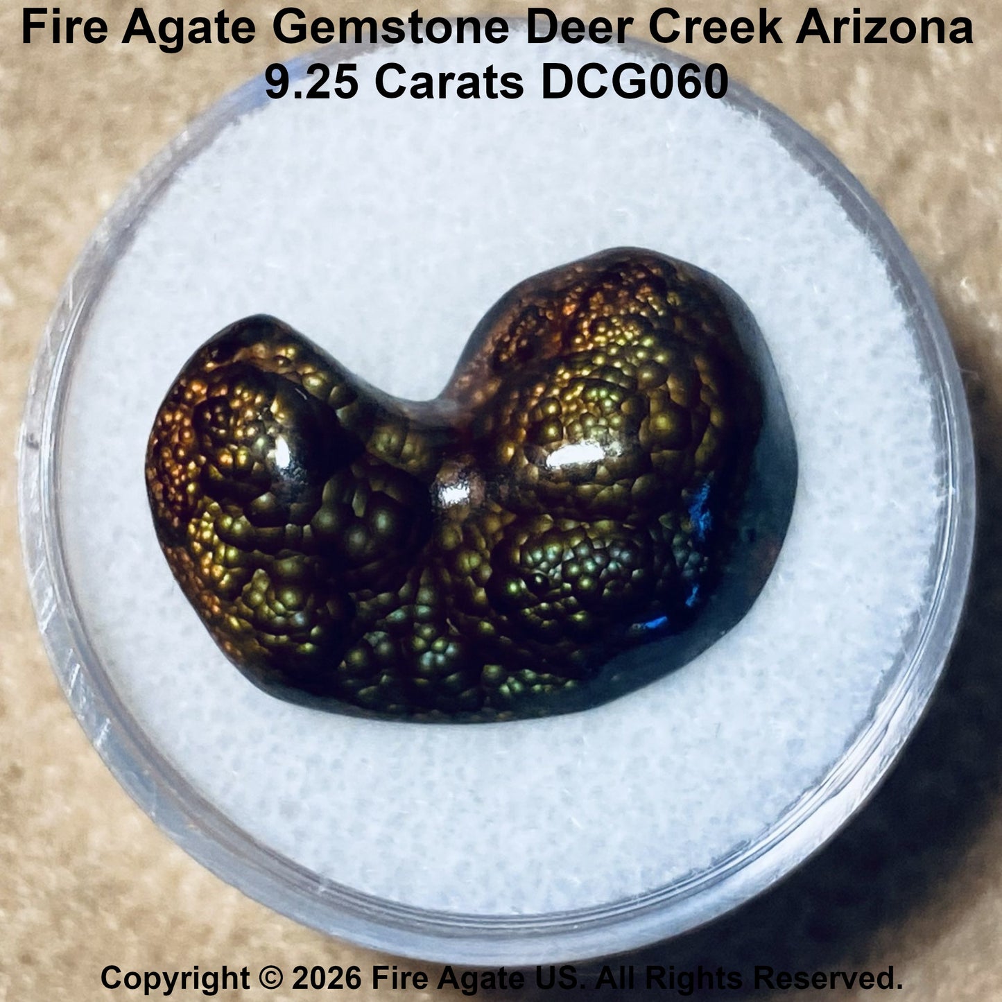 A 9.25 carat Fire Agate gemstone with a distinctive pinfire bubble texture, displayed in a clear round container on a textured insert.