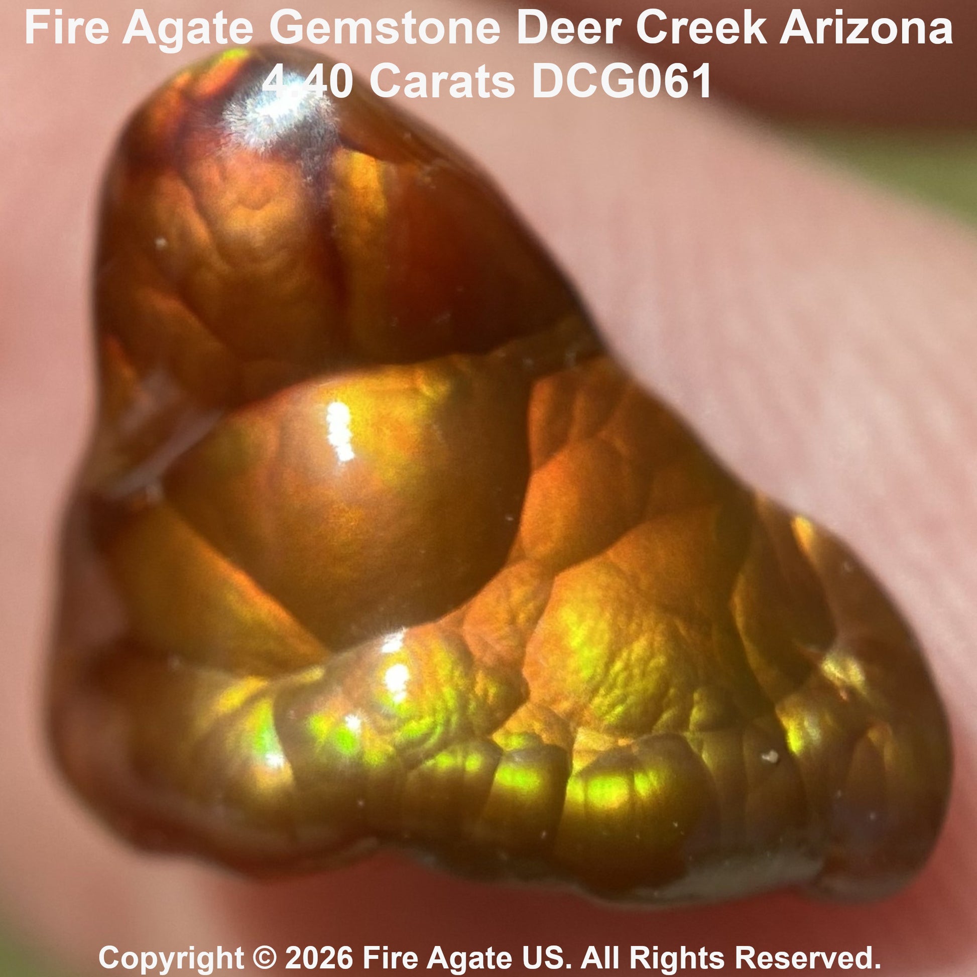 A close-up of a polished fire agate gemstone with a warm golden-brown body and vivid iridescent green flashes, held against a blurred skin background. Text at the top reads 'Fire Agate Gemstone Deer Creek Arizona 4.40 Carats DCG061' and a copyright notice appears at the bottom.