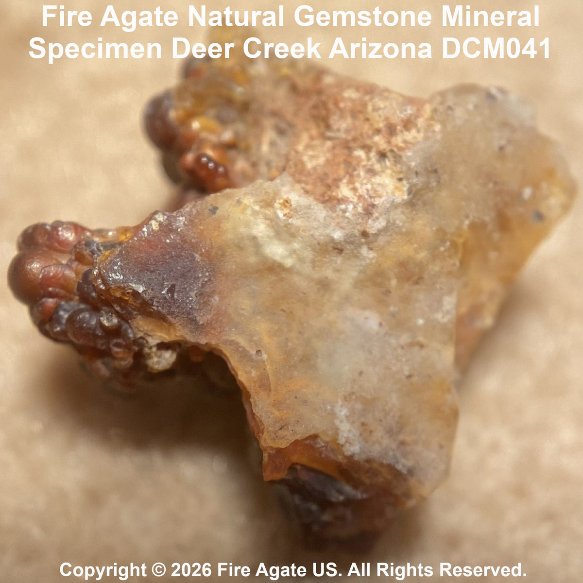 A natural fire agate gemstone mineral specimen with a rough, crystalline texture in translucent amber-brown and beige tones, shown on a tan background with text overlays identifying it as a Deer Creek Arizona specimen.