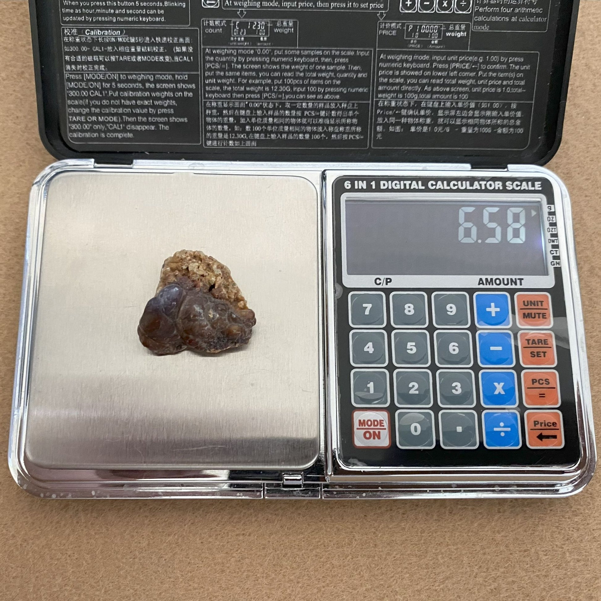 Digital calculator scale with a rock on it, displaying a weight of 6.58 grams.