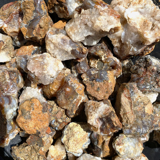 A close up pile of rough natural mineral specimens and fire agate rocks in earthy tones of brown, tan, cream, and gray.