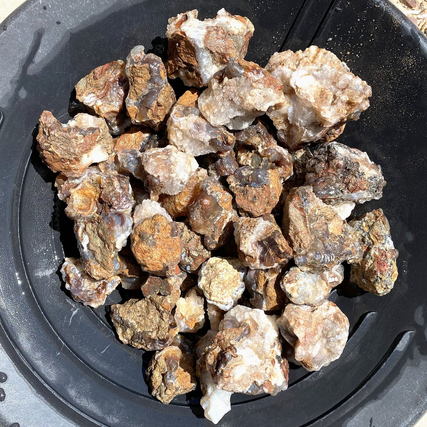 A pile of rough fire agate rock chunks with earthy brown, tan, and white crystalline textures, resting inside a black plastic bowl.
