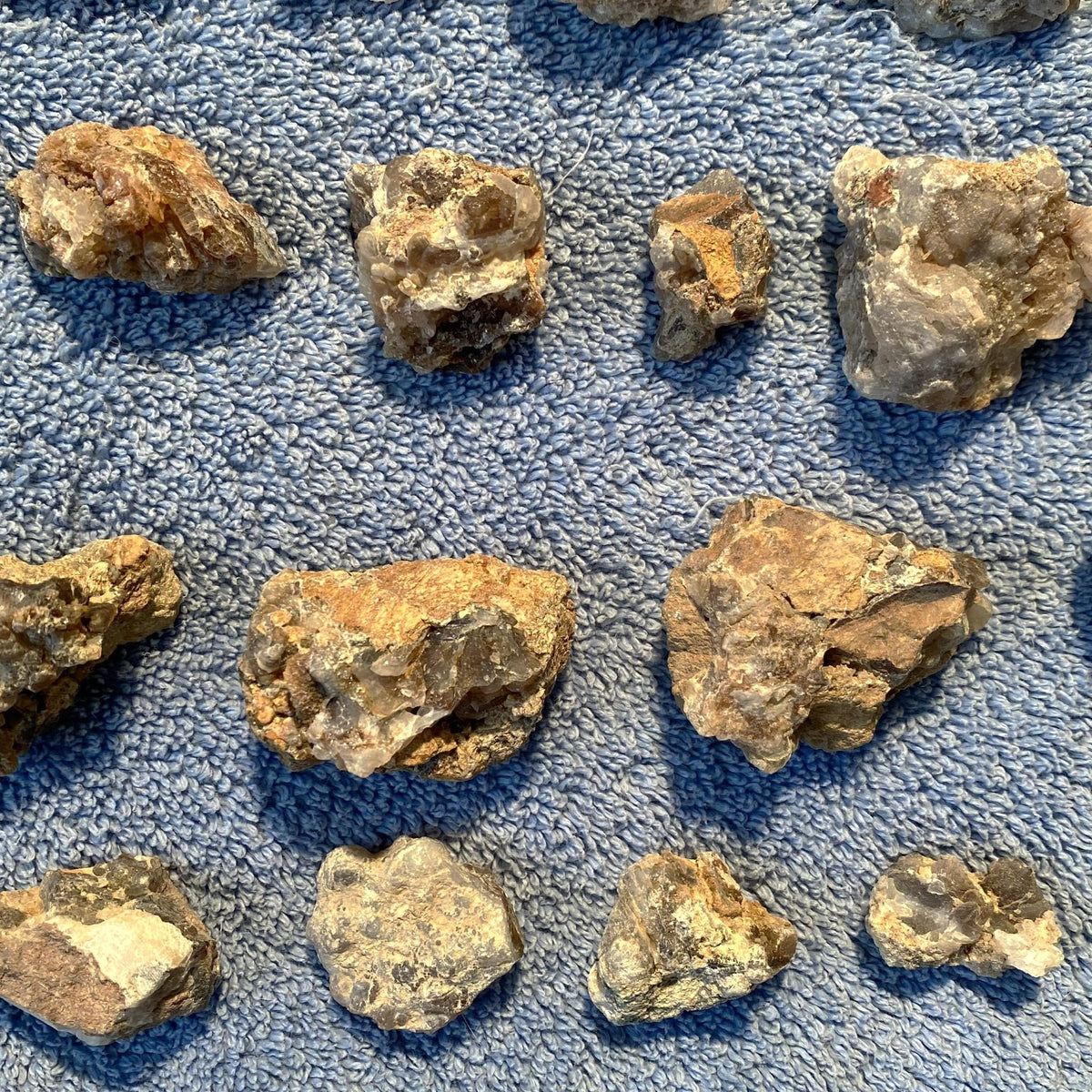 Several rough, natural-looking mineral or stone pieces in earthy brown, tan, and gray tones arranged on a textured blue fabric background.