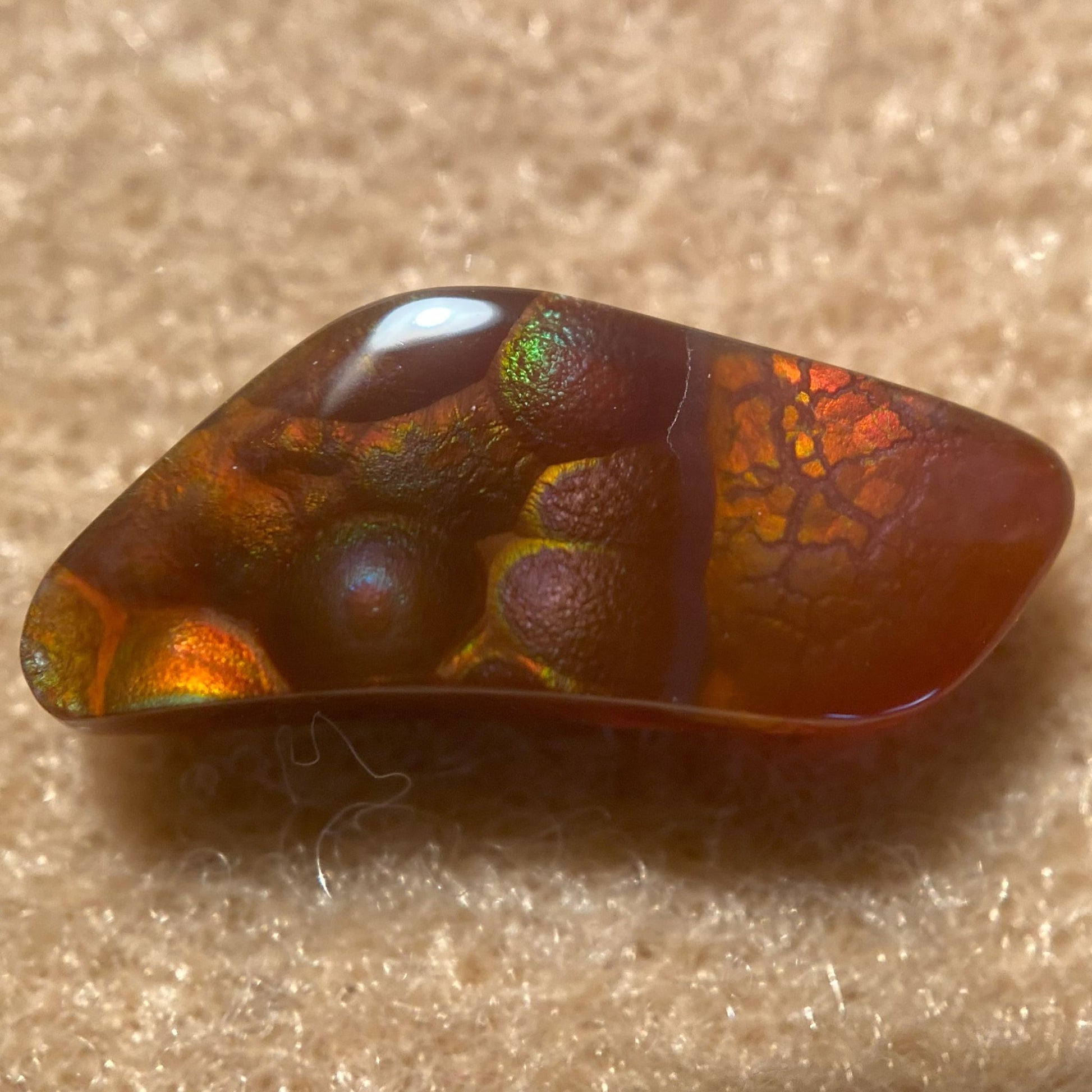 Polished Fire Agate Gemstone with iridescent colors on a beige background