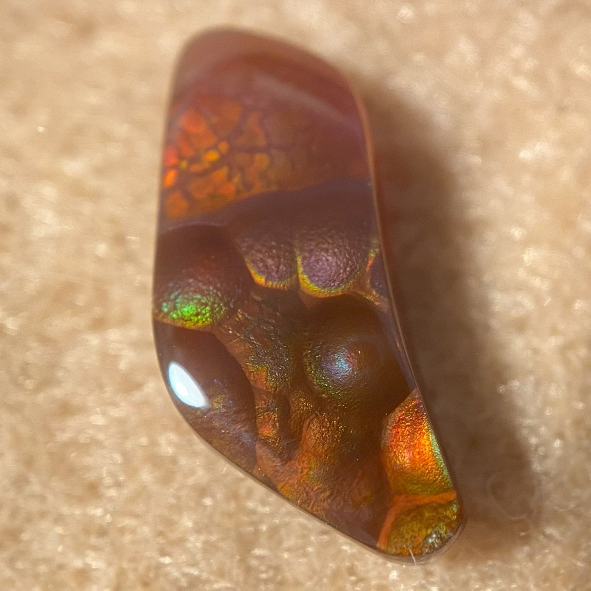 Close-up of a colorful Fire Agate Gemstone with iridescent patterns on a beige background