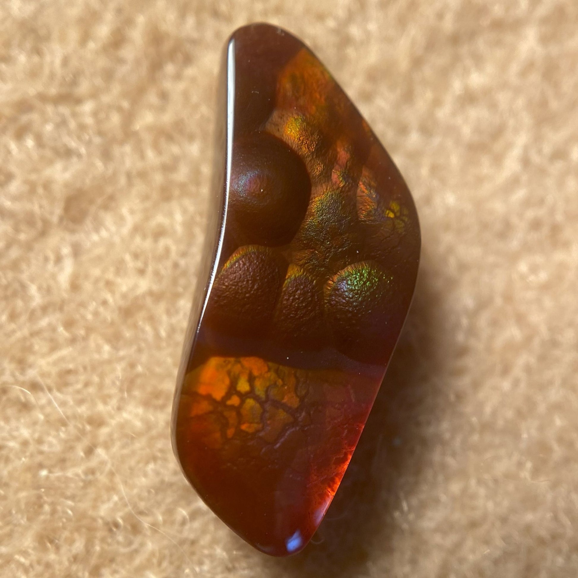 Polished Fire Agate Gemstone with multicolored patterns on a beige background