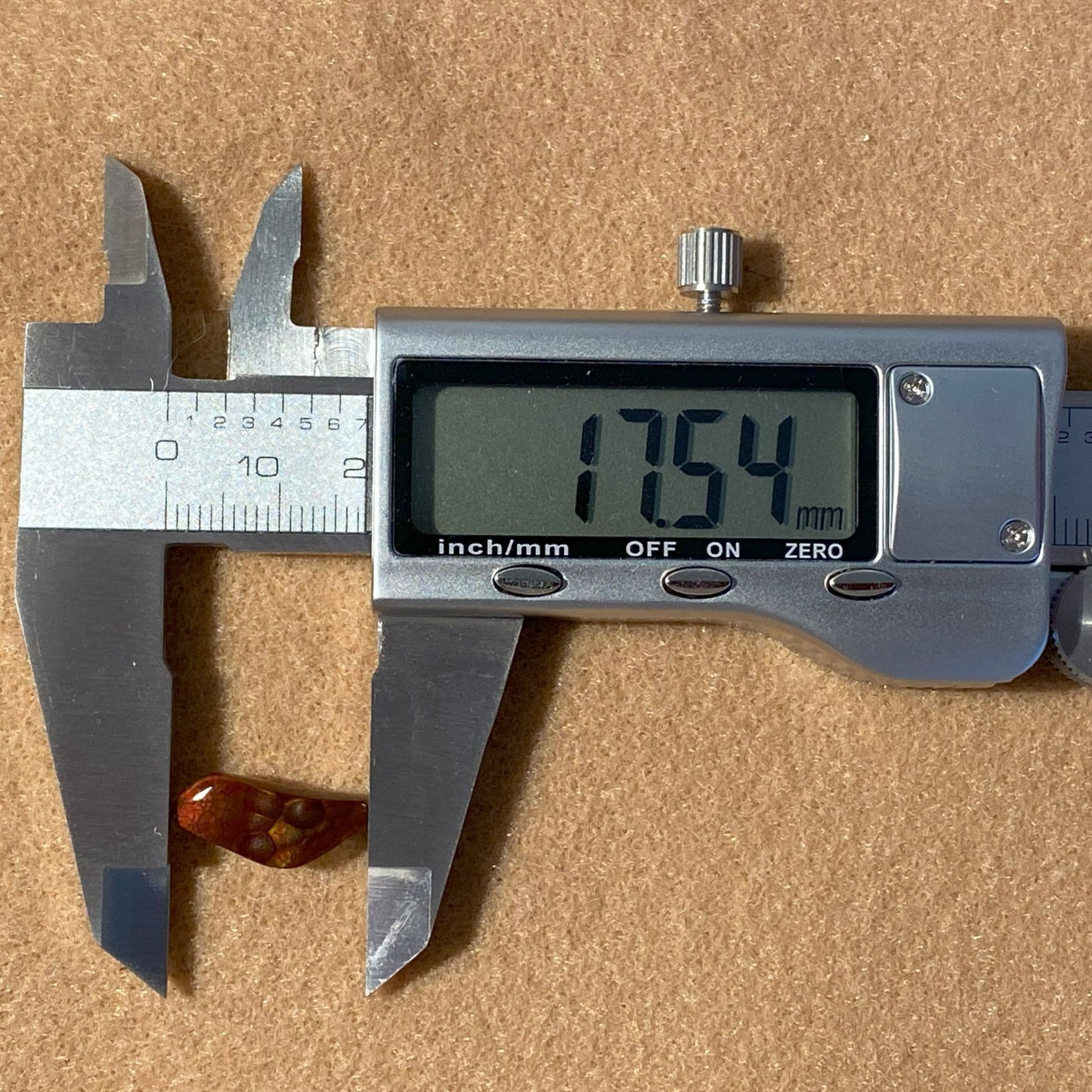 Digital caliper measuring a Fire Agate Gemstone with a displayed measurement on a brown background