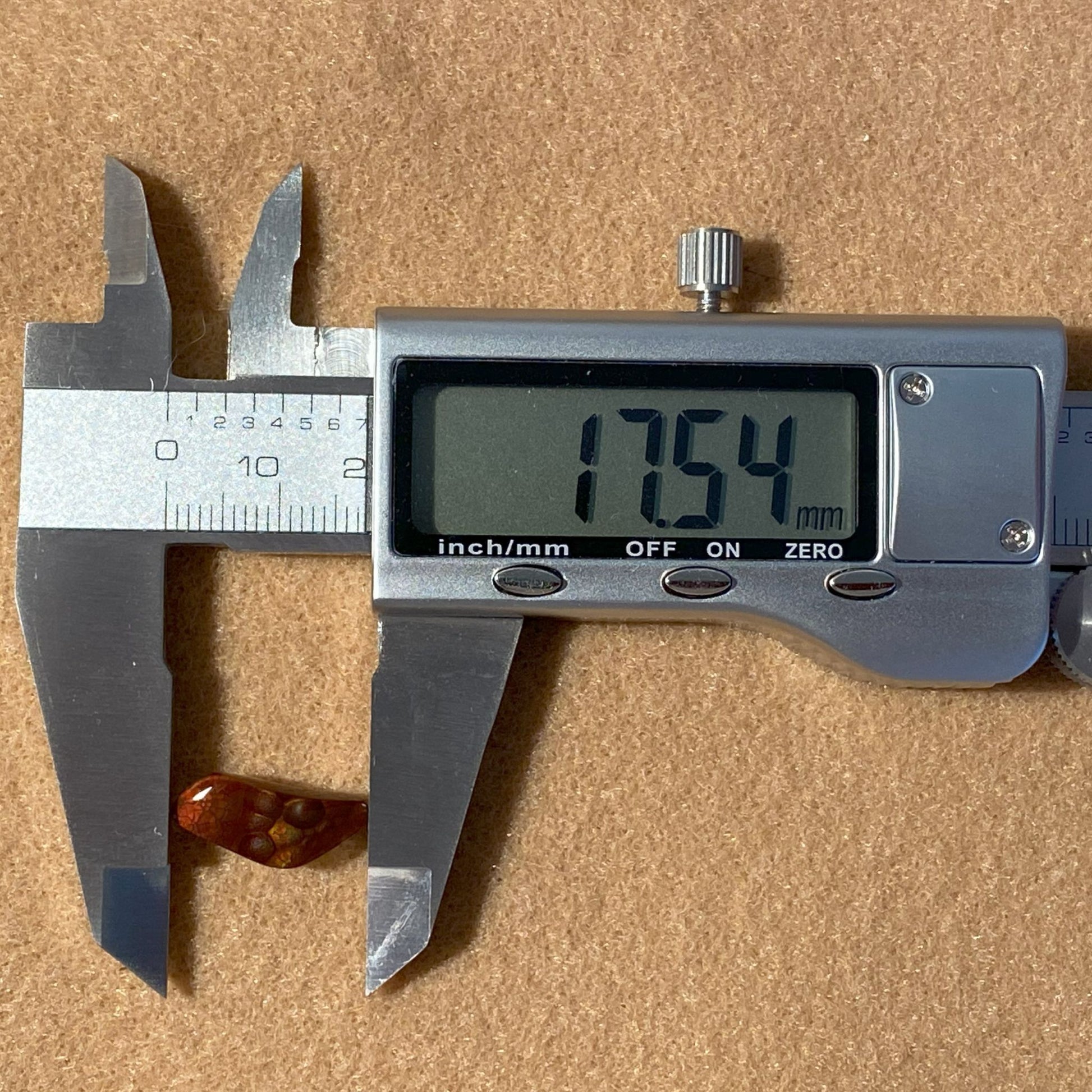 Digital caliper measuring a Fire Agate Gemstone with a displayed measurement on a brown background