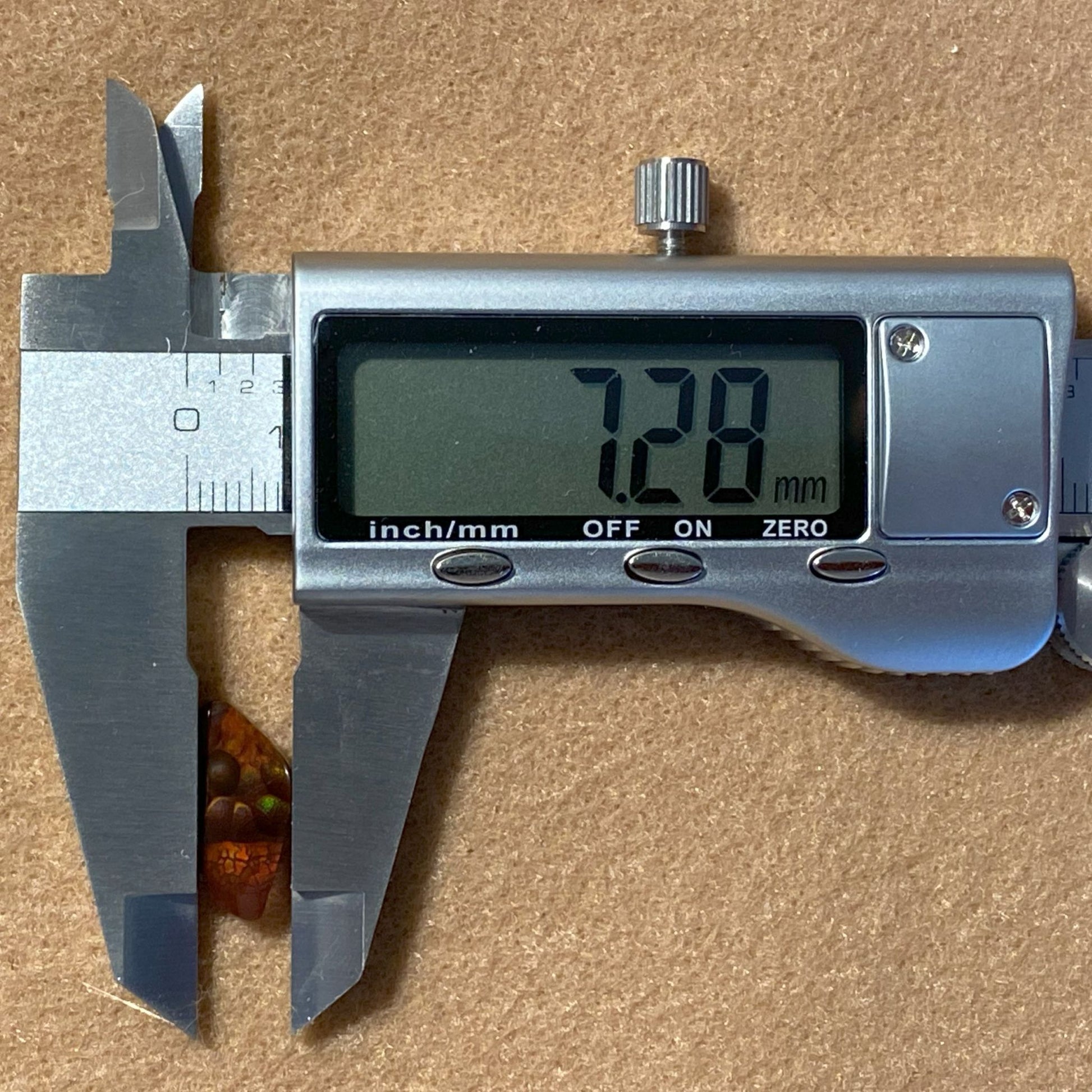 Digital caliper showing measurement of 7.28 mm on a brown background