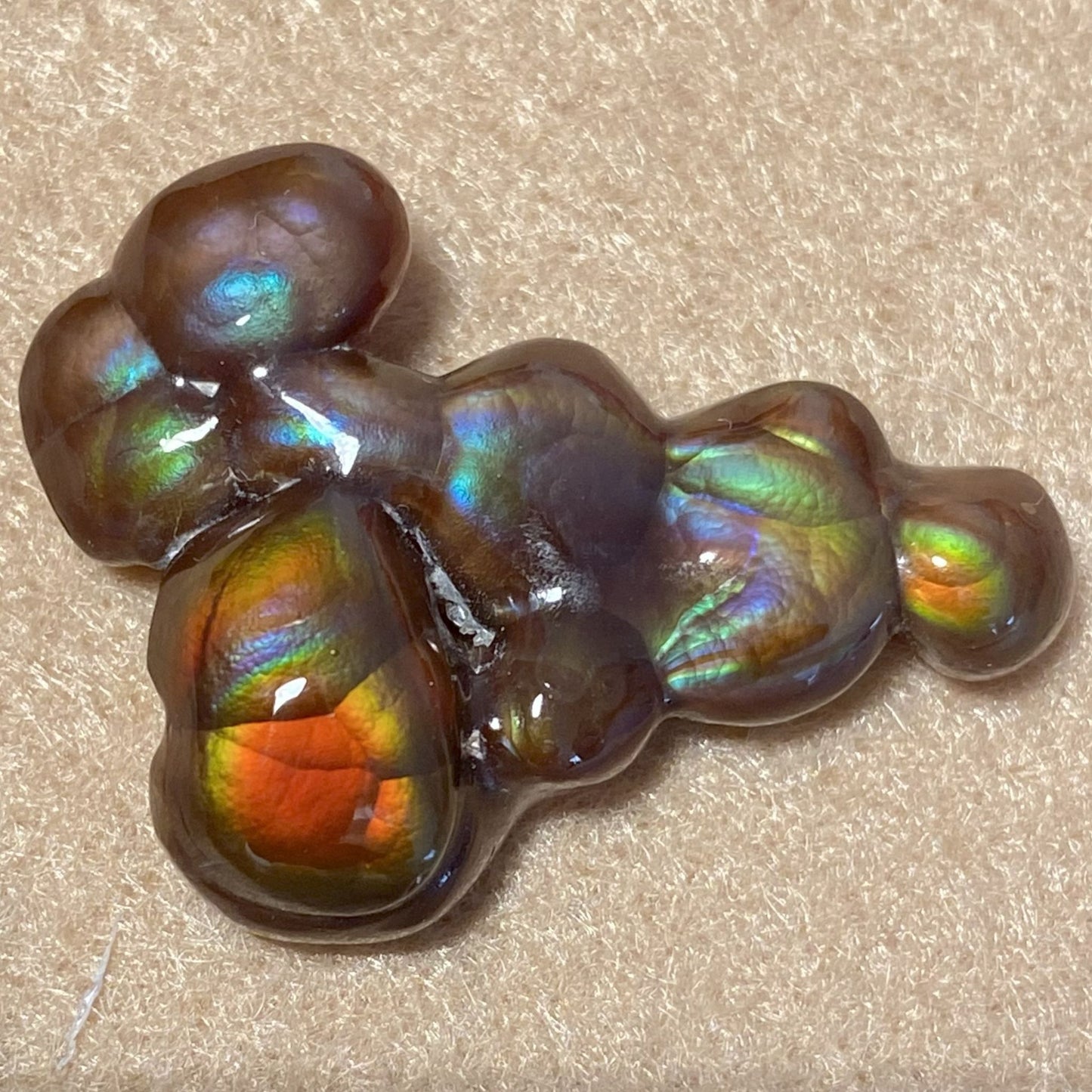 Multicolored Aguascalientes Fire Agate Gemstone with iridescent sheen on a beige background