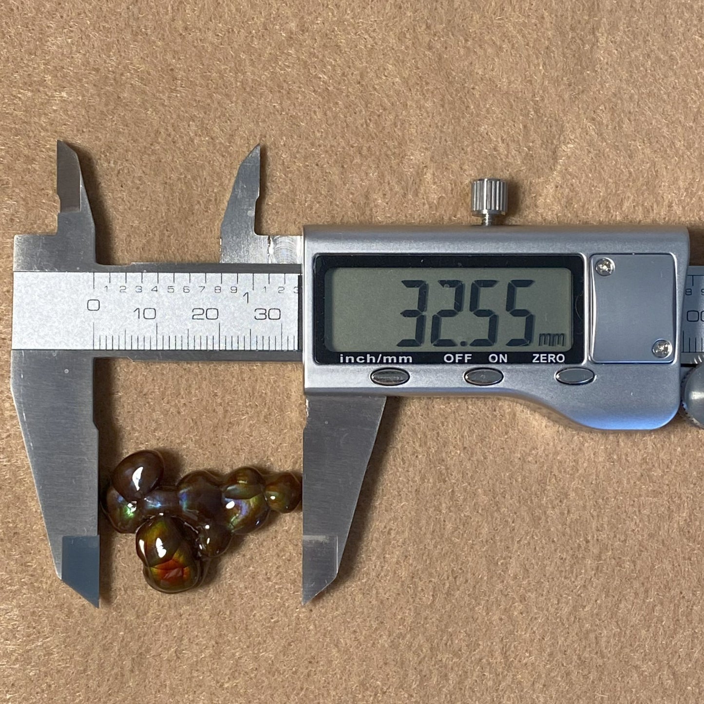 Digital caliper measuring a Aguascalientes Fire Agate Gemstone on a brown surface