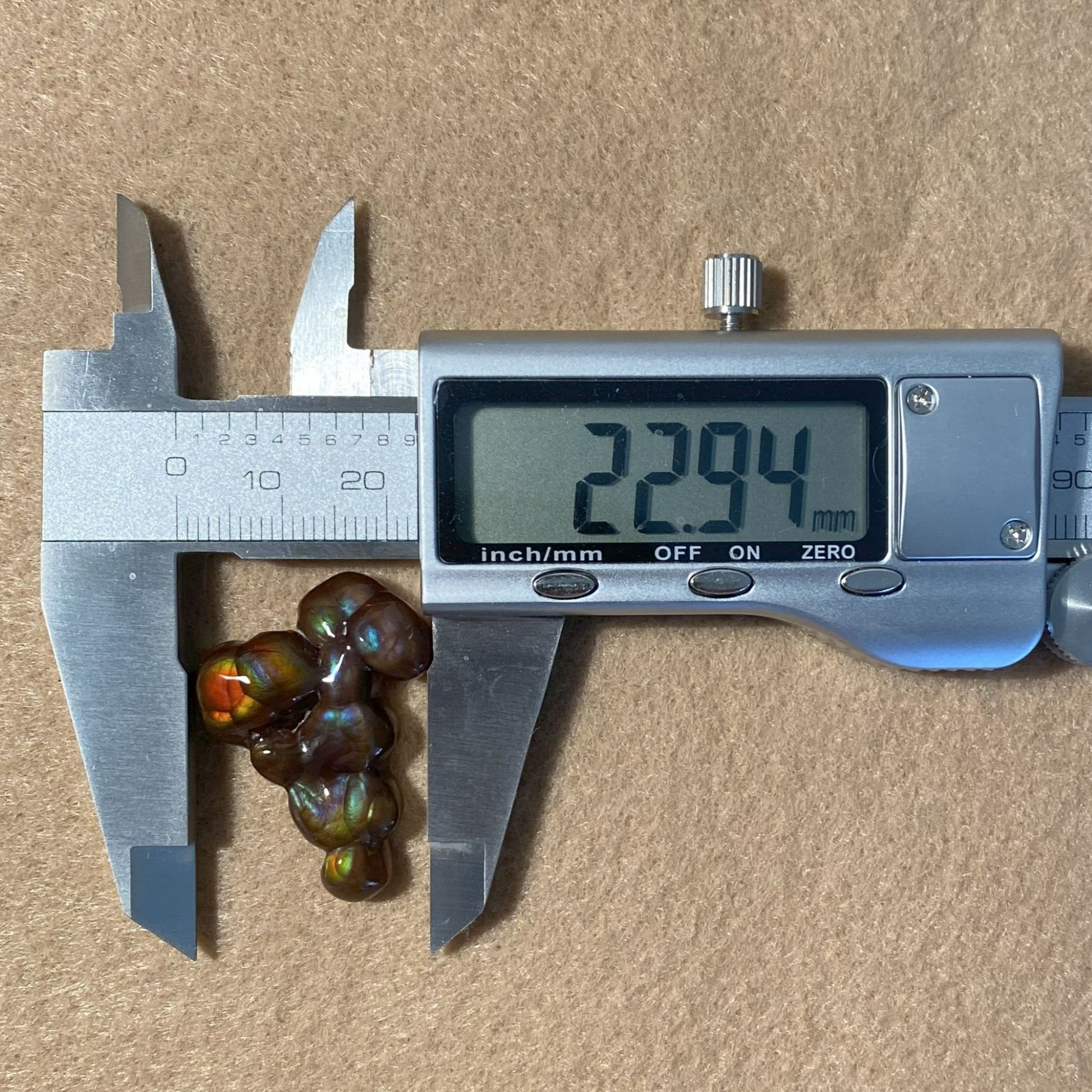 Digital caliper measuring a Aguascalientes Fire Agate Gemstone on a beige background