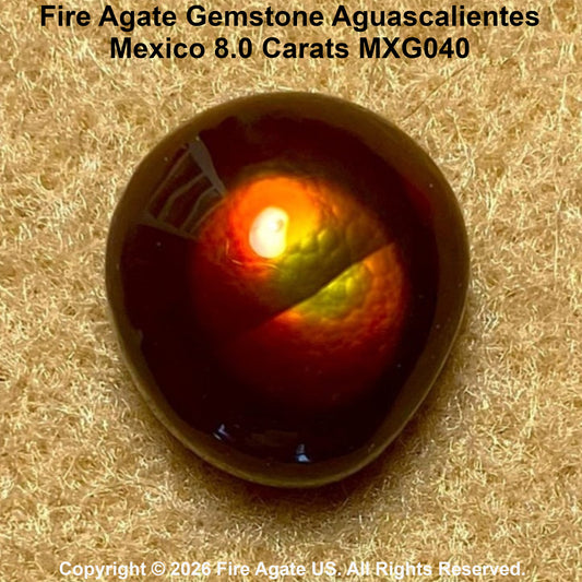 A 8.0 carat Fire Agate gemstone with a rounded, polished dome shape, displayed on a textured beige surface.